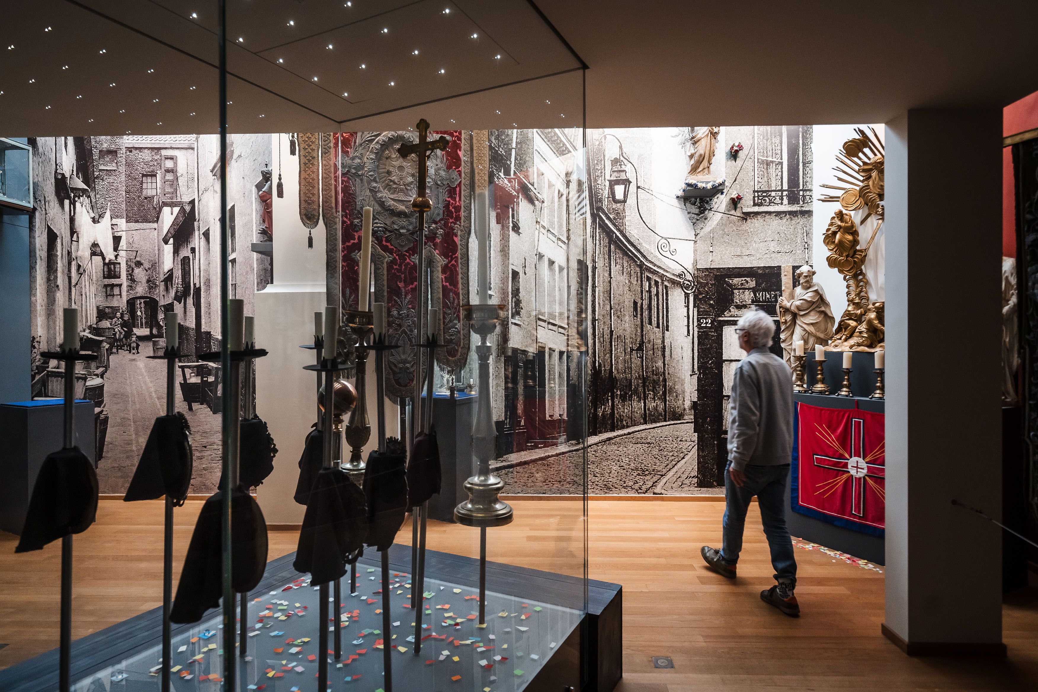 Tentoonstellingsruimte in een museum met grote zwart-witfoto’s aan de wanden. Bezoekers wandelen door de zaal langs vitrines en informatiepanelen. De ruimte is modern ingericht en verlicht.
