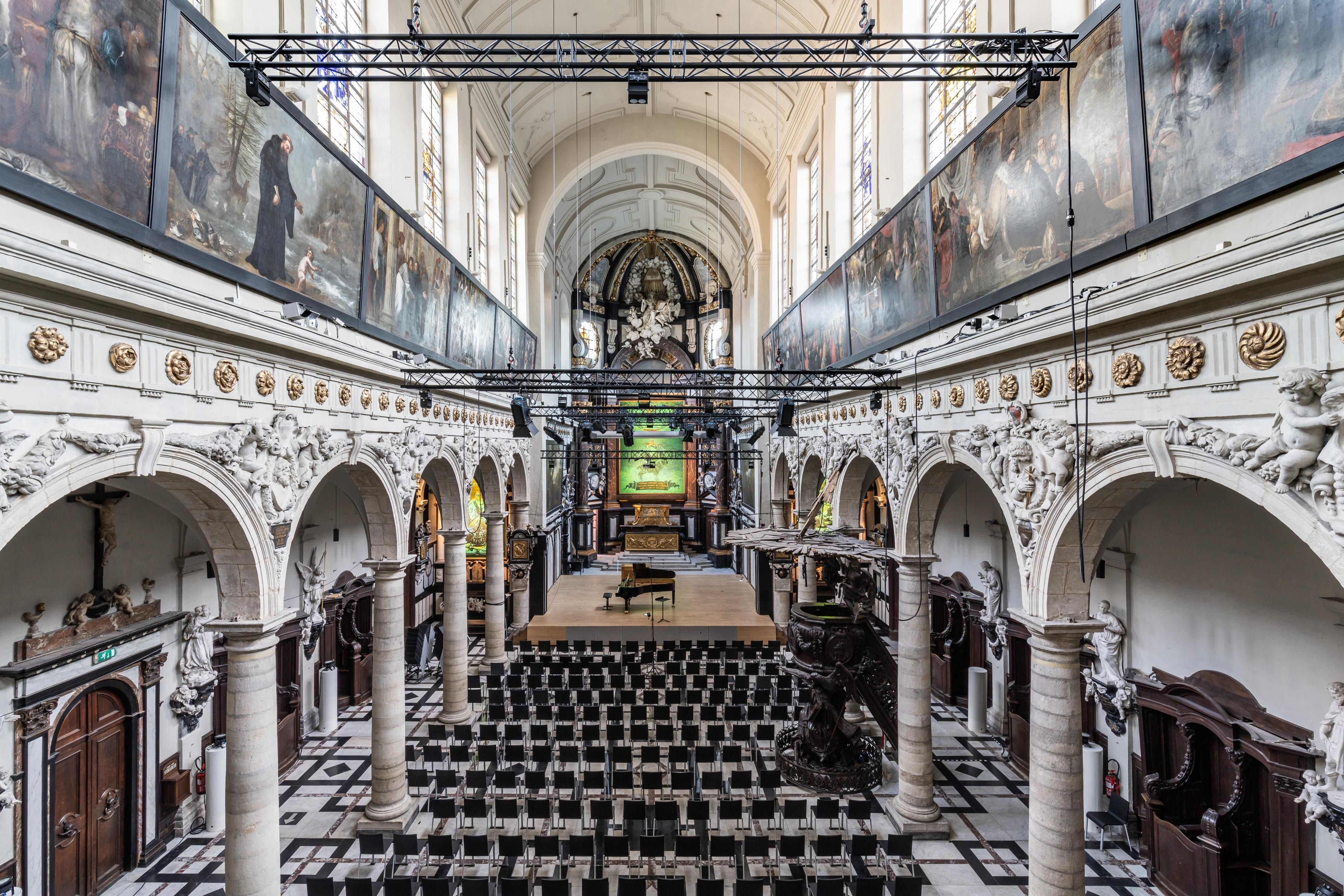 Vooraanzicht van het podium met stoel ervoor in een ruimte die barok uitstraalt. Aan het plafond hangen spots om lichttechniek toe te passen.