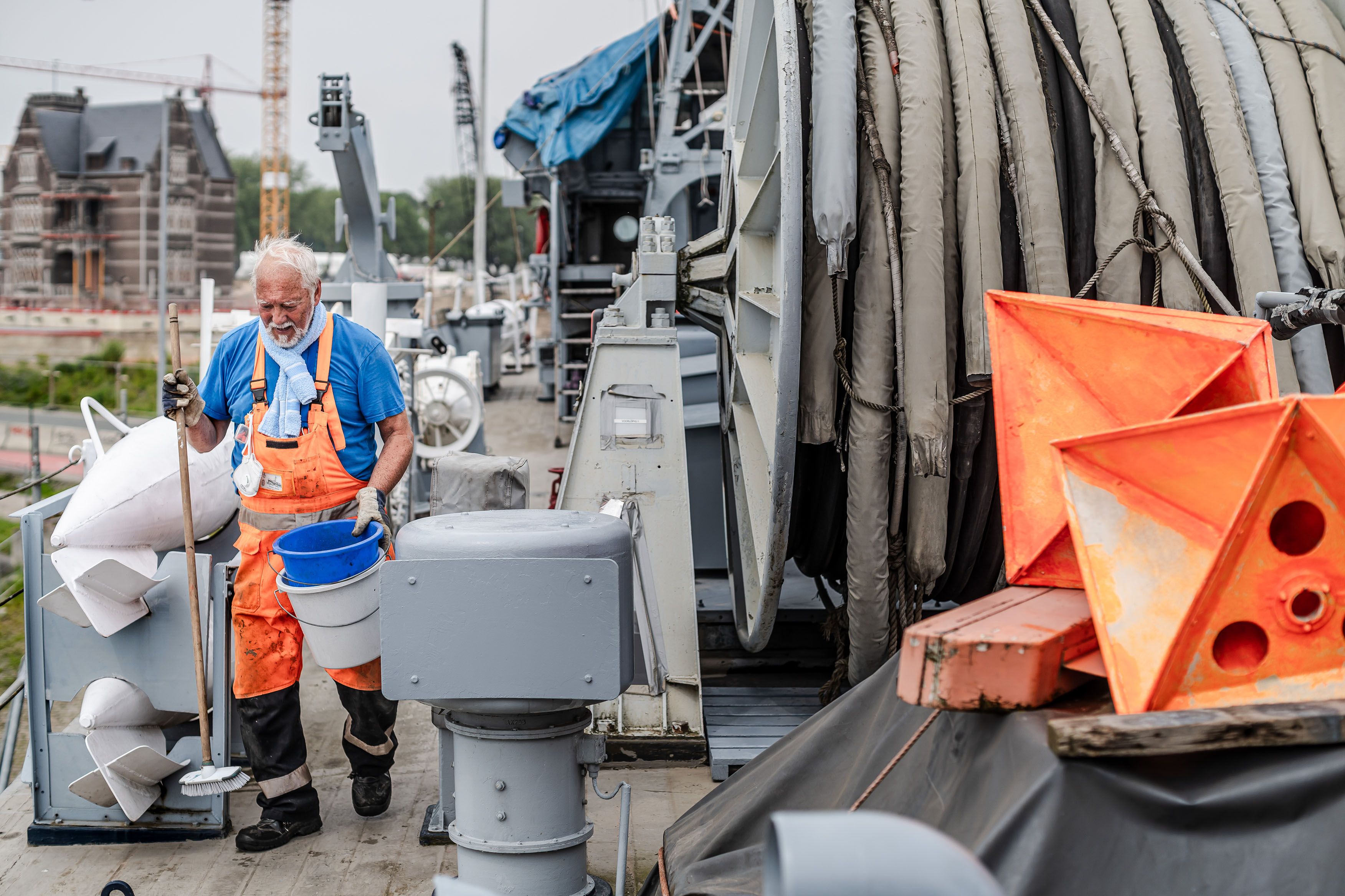 Man met fluo-oranje overal poetst het dek van een schip