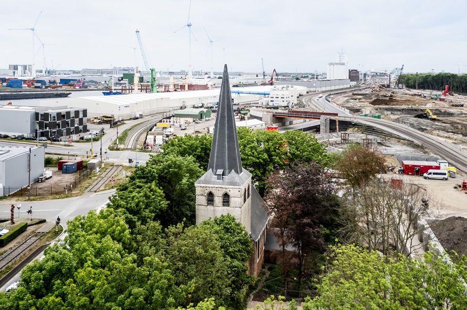 Lager gelegen kerktoren, omringd door bomen en door de haven