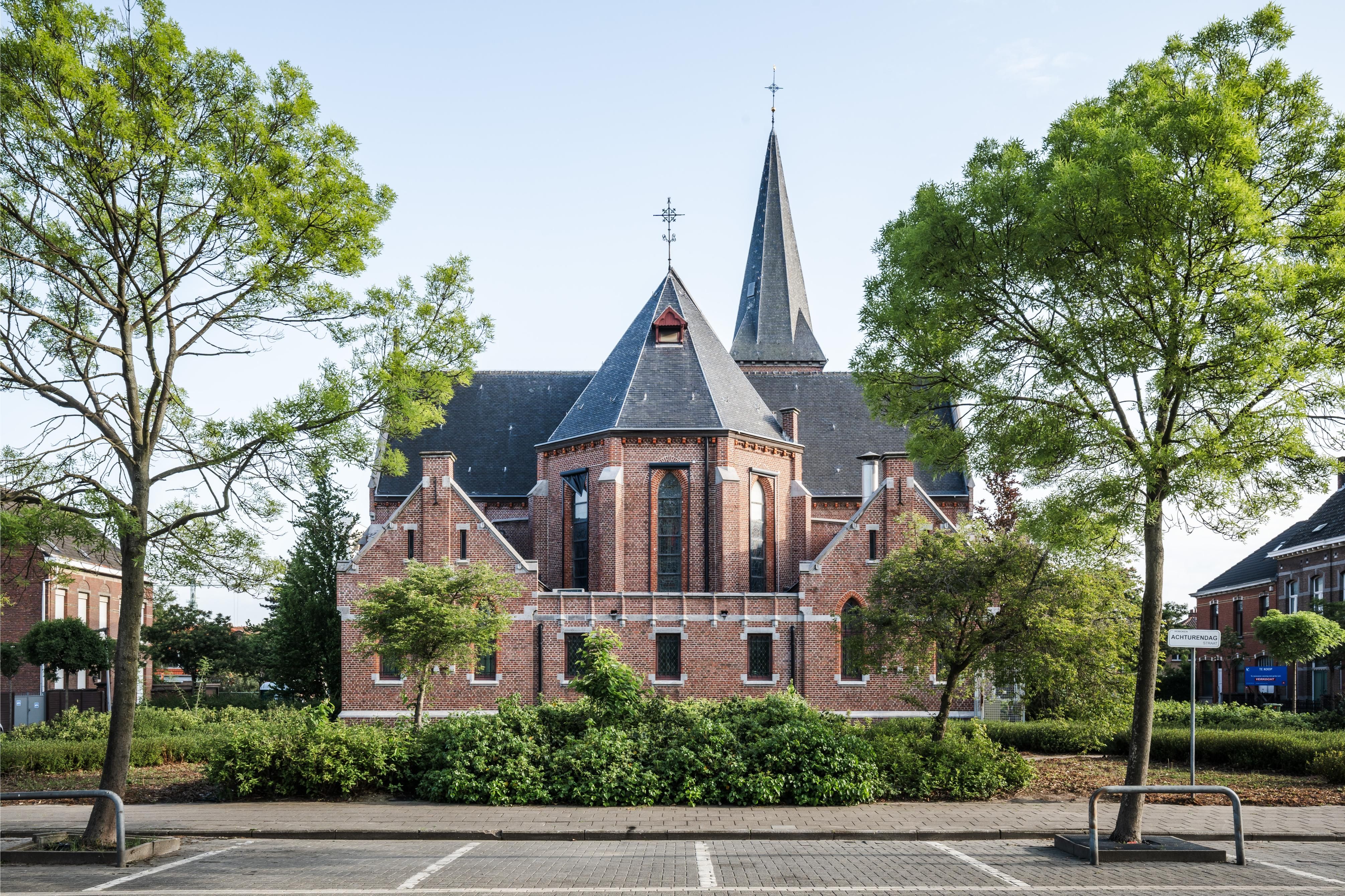 Achtergevel van Sint-Jozefkerk met 2 bomen en lage struiken.