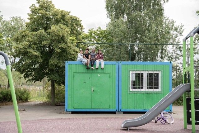 Groene container waarop 4 jongeren zitten en een glijbaan.