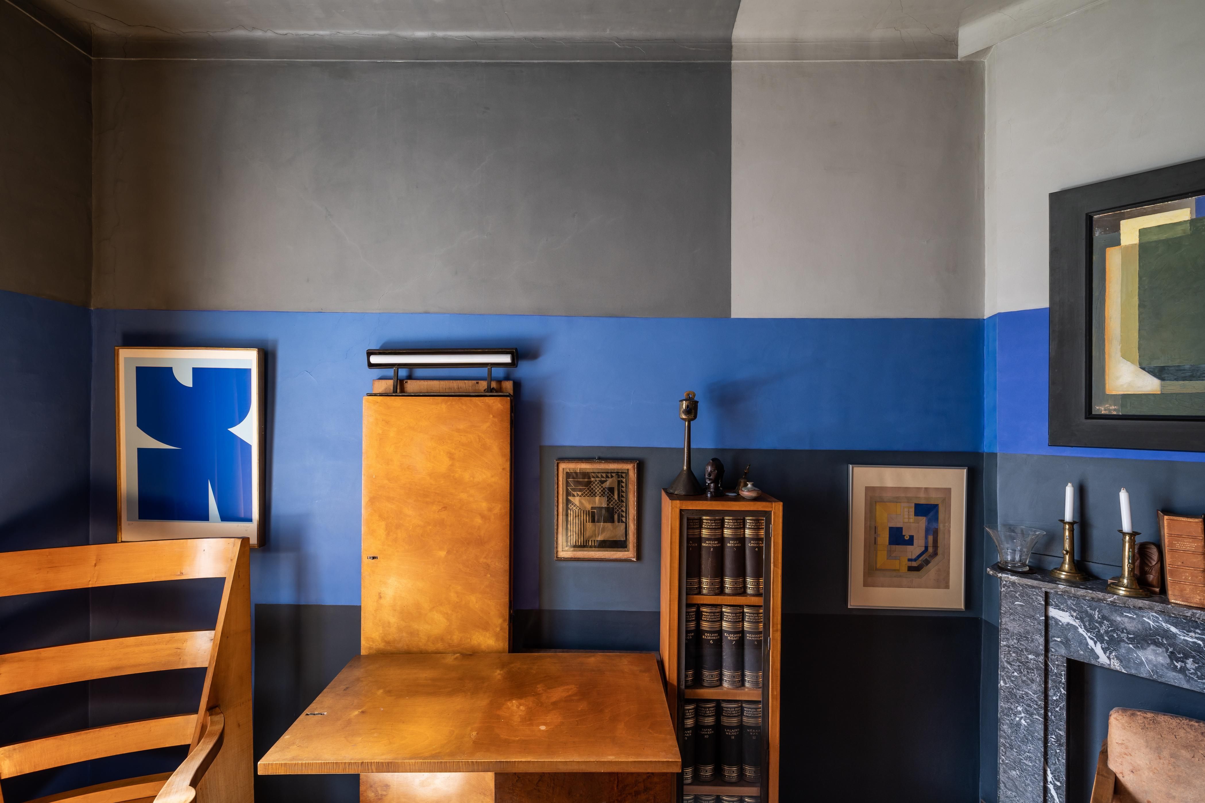 Ruimte met houten kasten, een blauw schilderij en wanden in blauw en grijs.