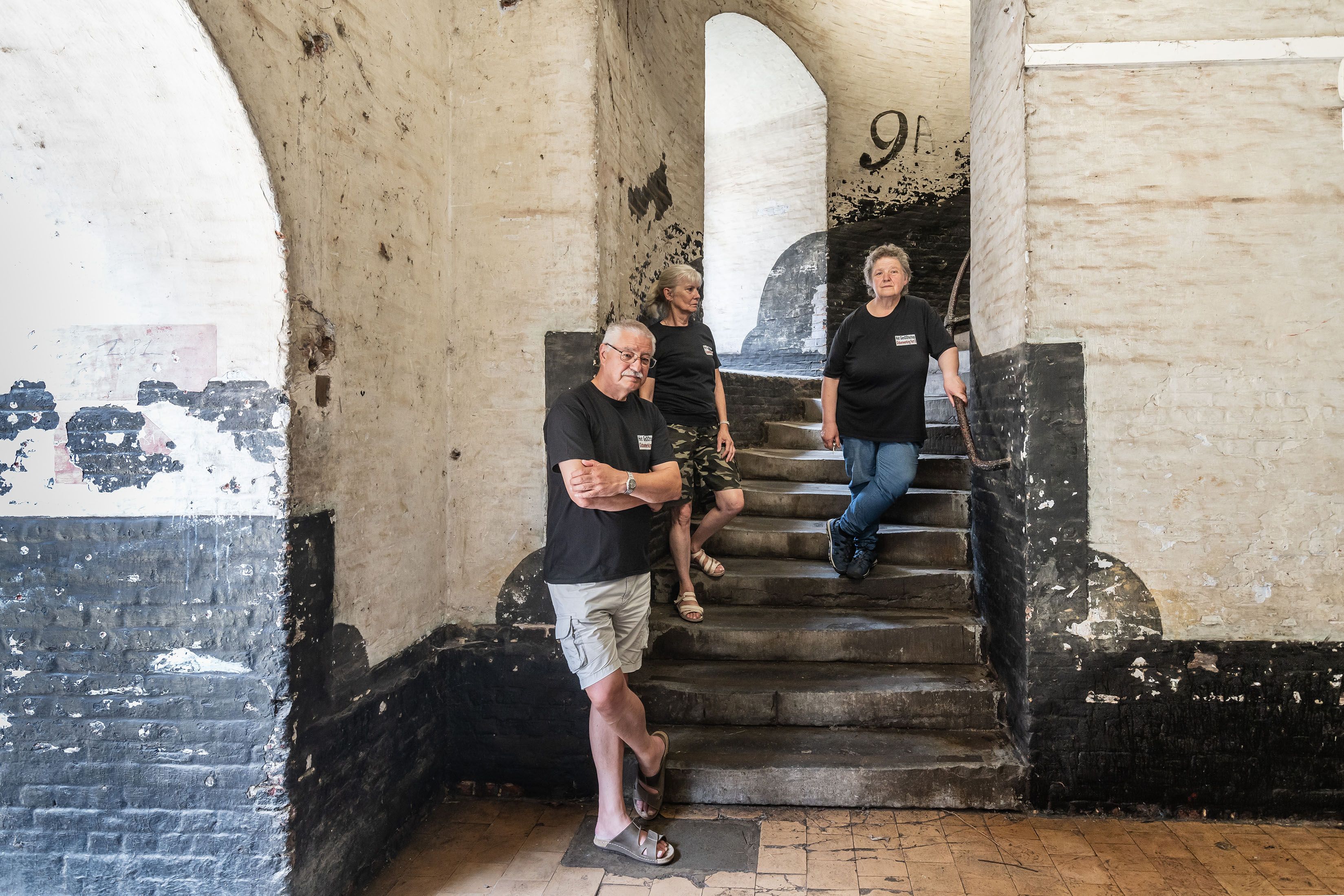 1 vrouw en 2 mannen staan op de trap en leunen tegen een muur in fort 8.