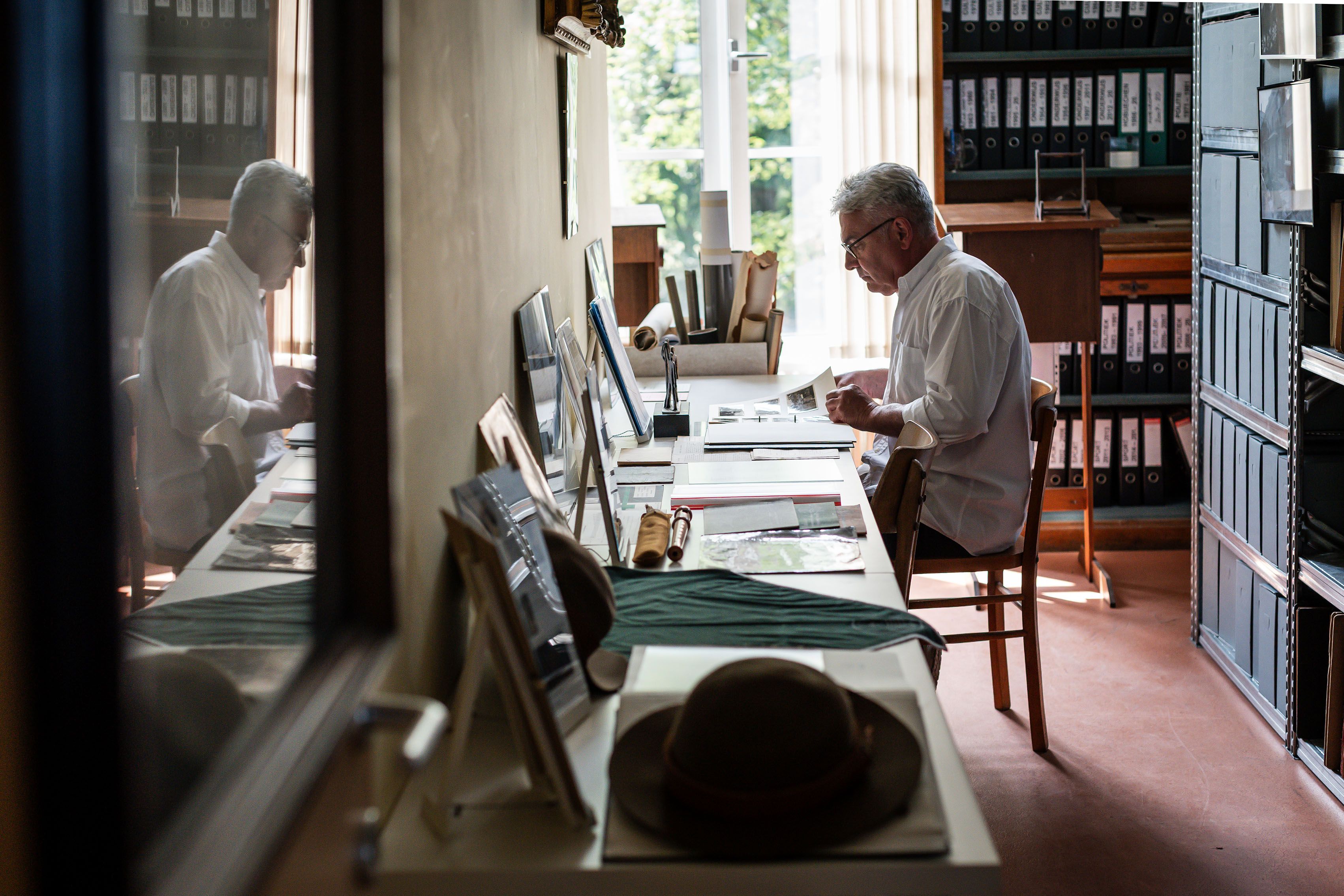 Man van middelbare leeftijd zit aan een bureau in een archiefzaal.