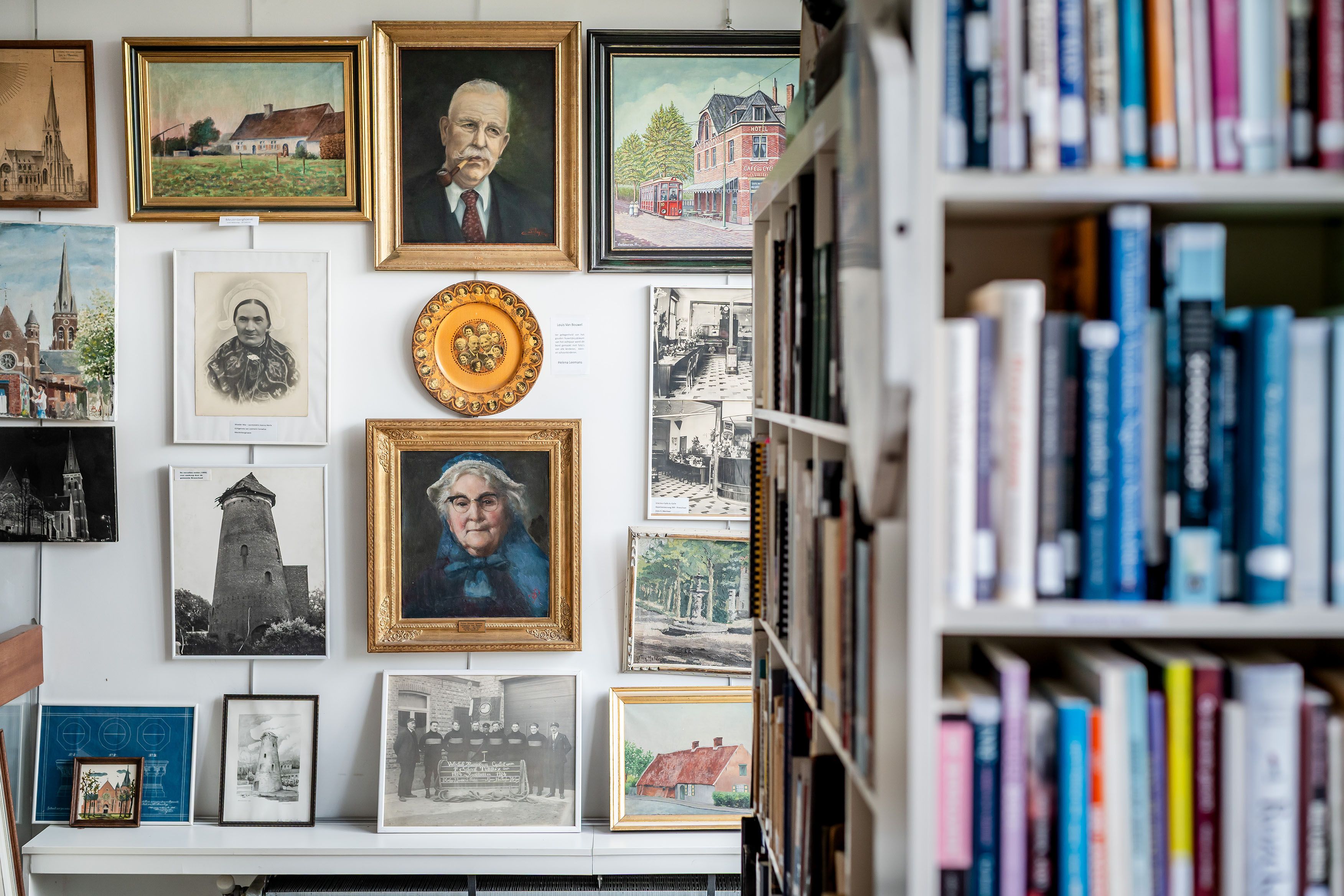 Zicht op een muur met oude portretten en dorpsgezichten in het wijkcentrum Sint-Mariaburg met rechts nog een stukje van de bibliotheek.