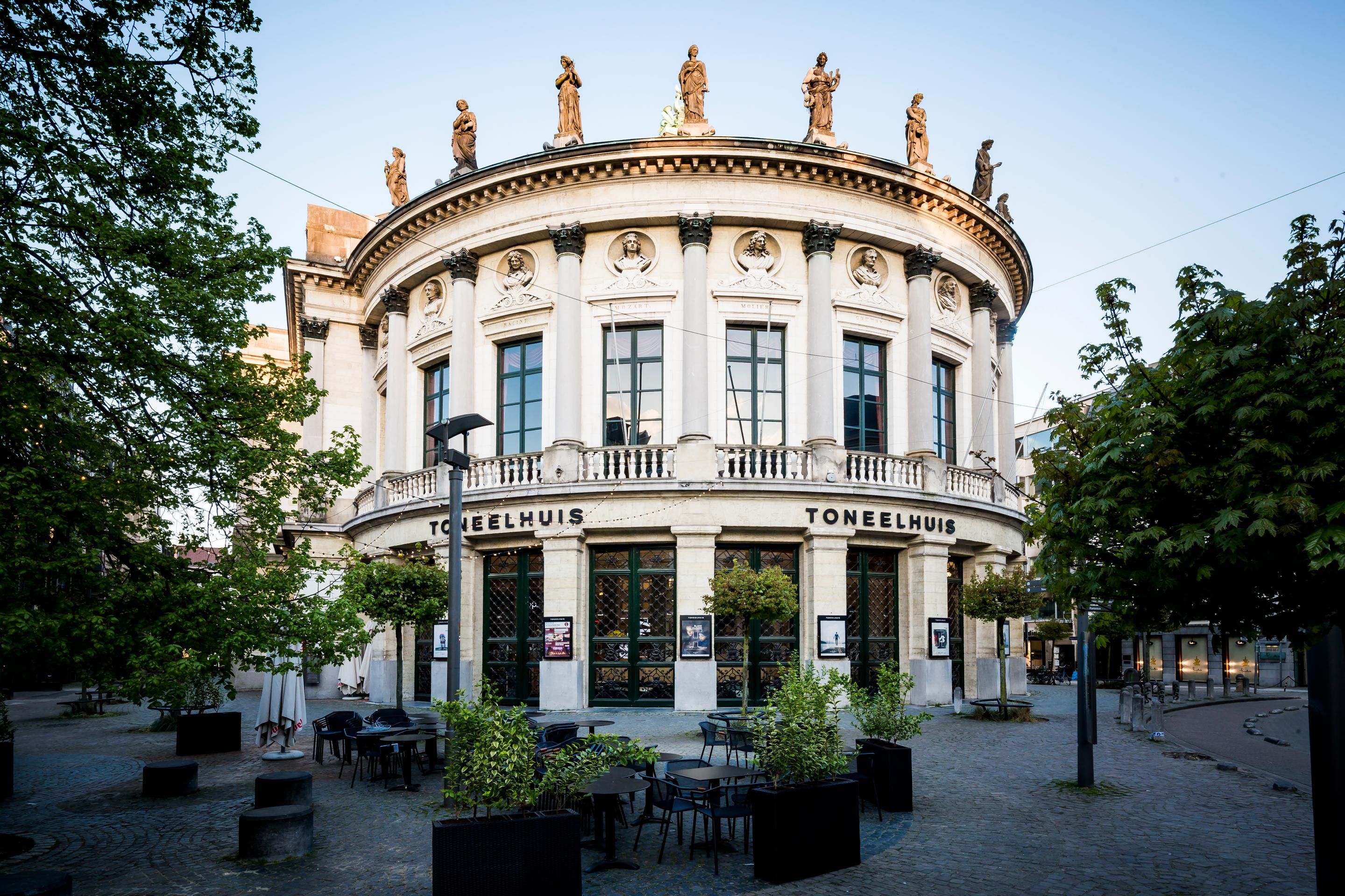 Hoe het gebouw er langs de straatkant uitziet: een wit rond gebouw ramen en met gouden details op het dak. 