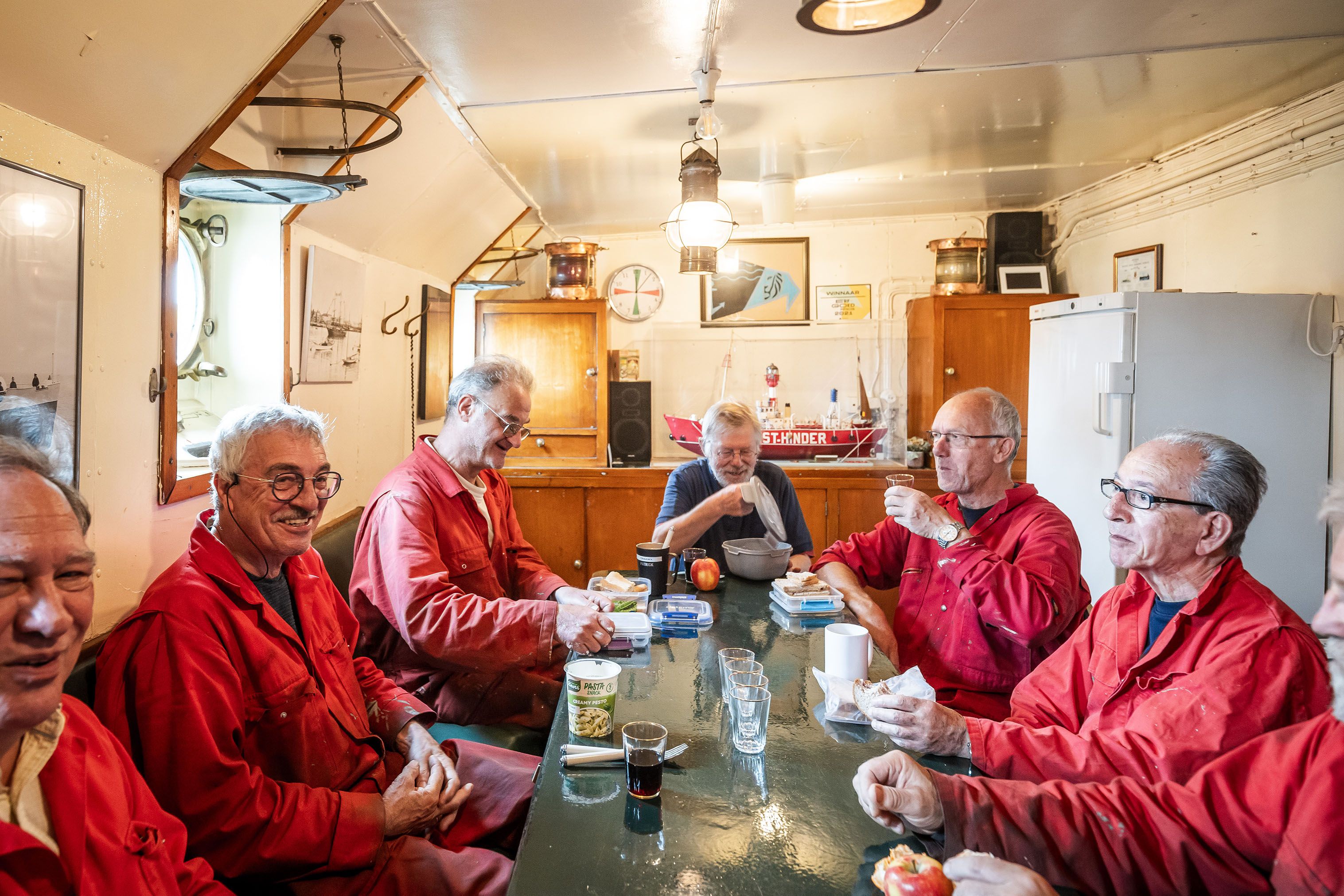 Vrijwilligers in rode overalls zitten rond een tafel in de Westhinder.