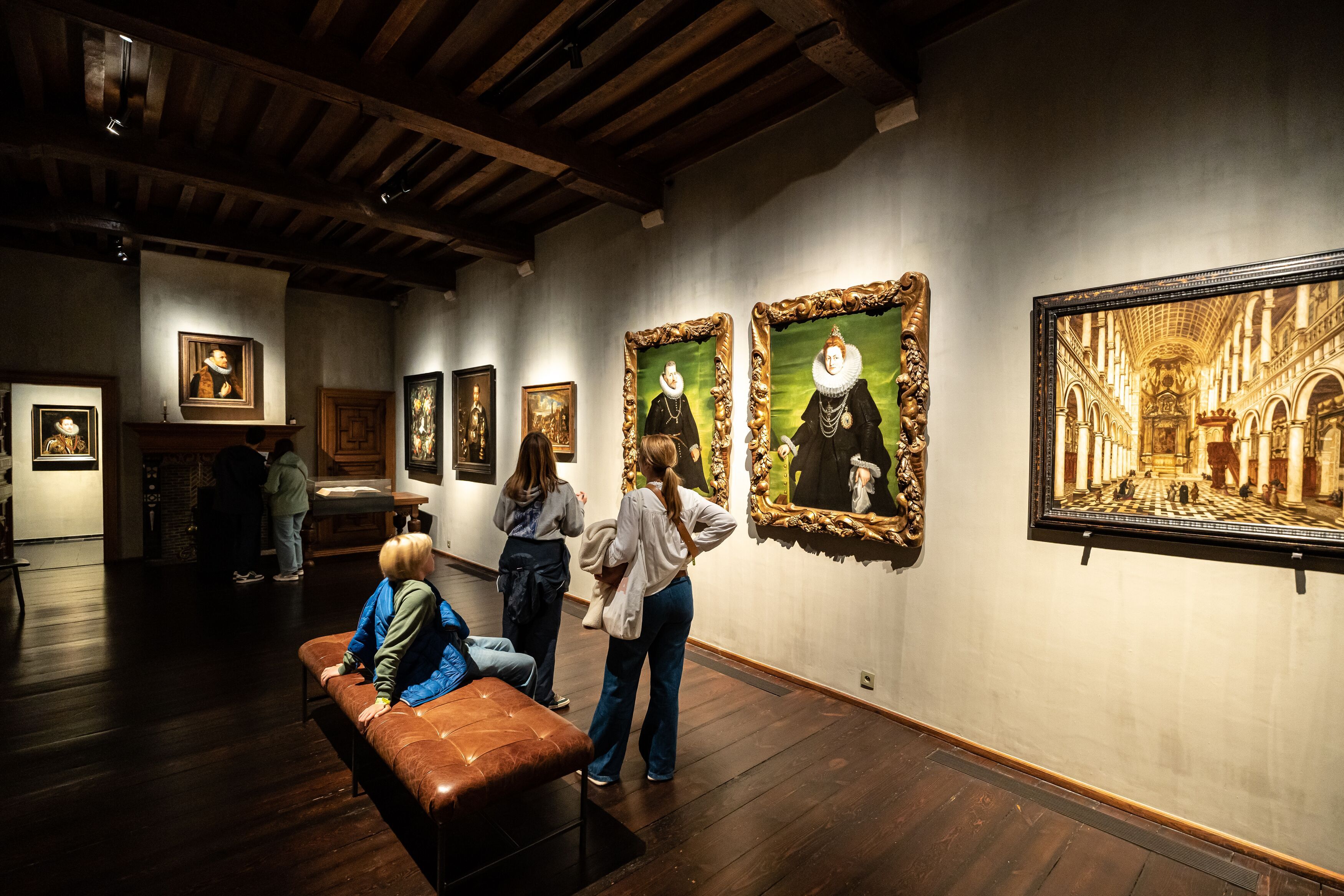 Beeld van binnen het museum. Bezoekers kijken naar schilderijen op de muur.