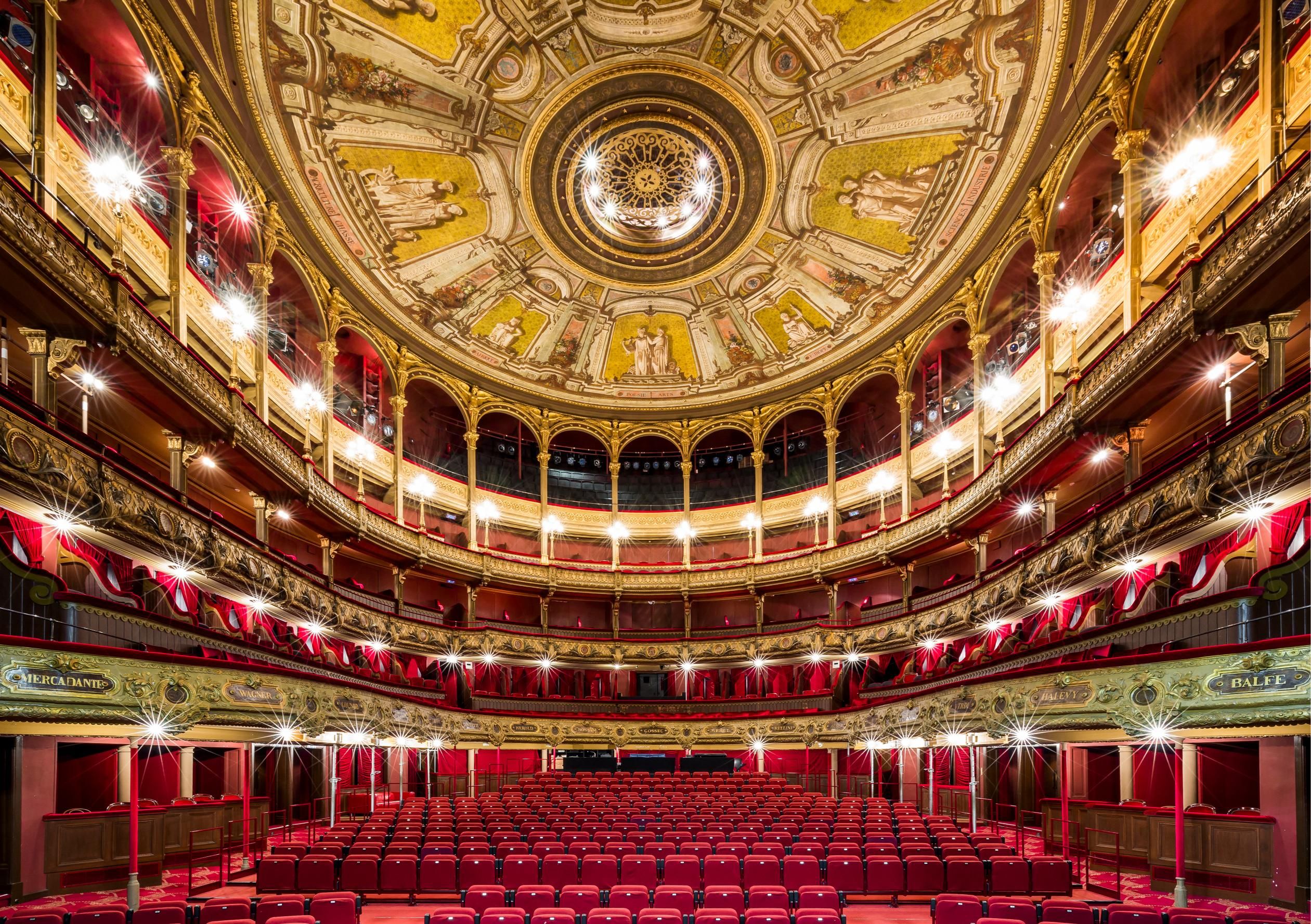 Foto vanop het podium richting zaal met rode stoelen en goud aan het plafond. 
