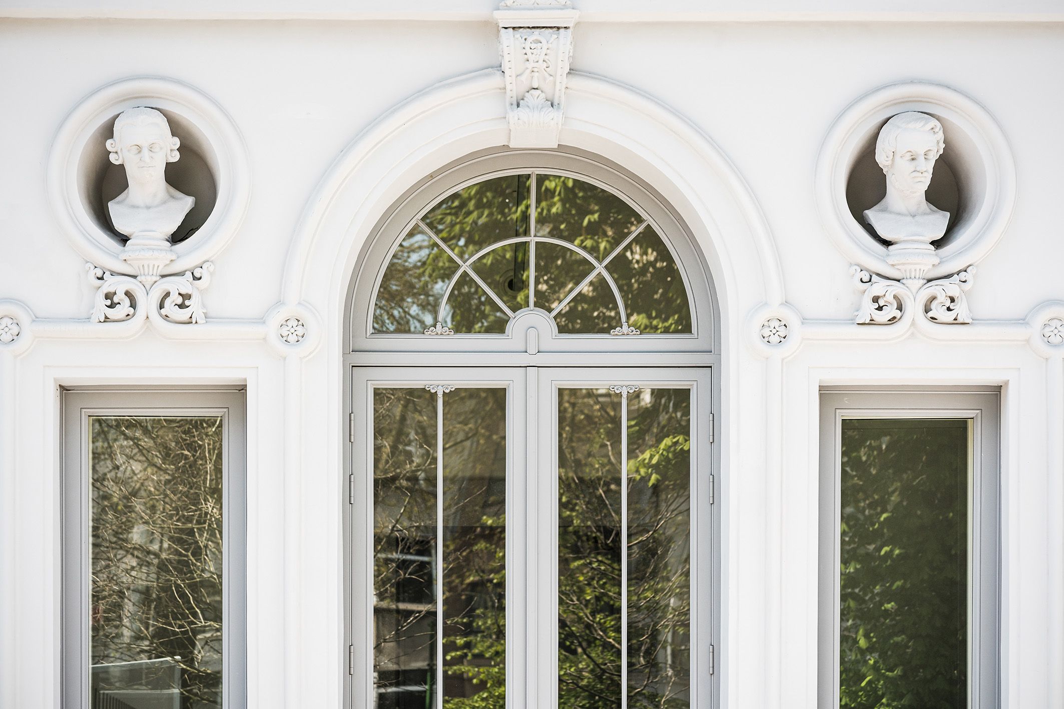 Detail van een dubbele deur met glas en 2 borstbeelden boven de zijramen.