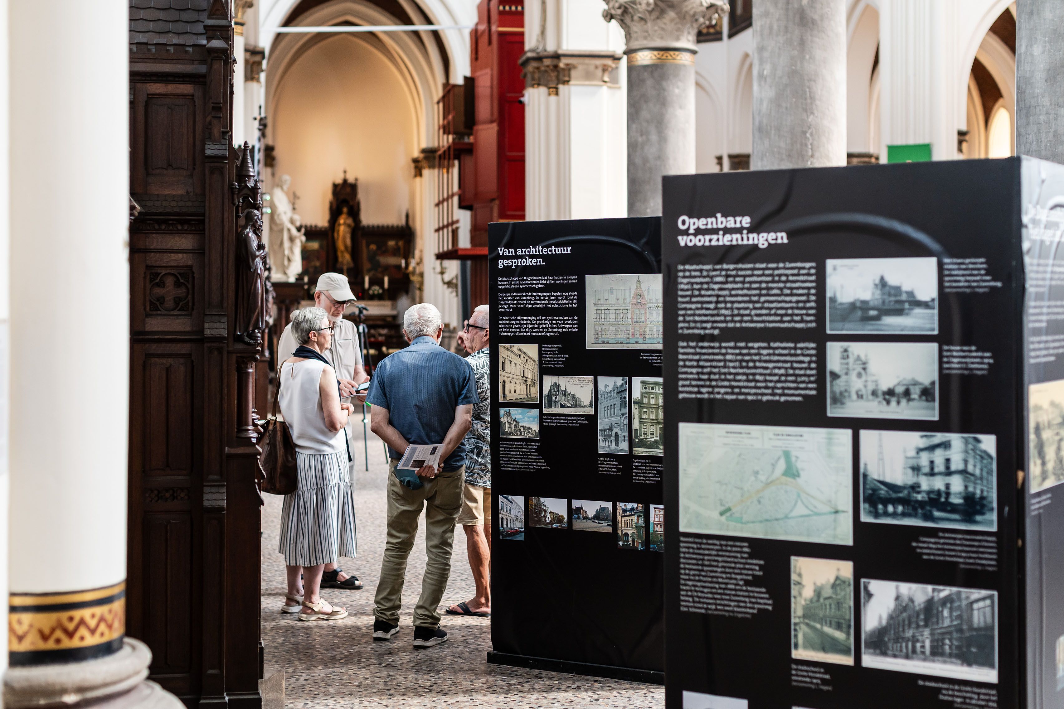 4 mensen praten met elkaar naast tentoonstellingspanelen in de Sint-Norbertuskerk