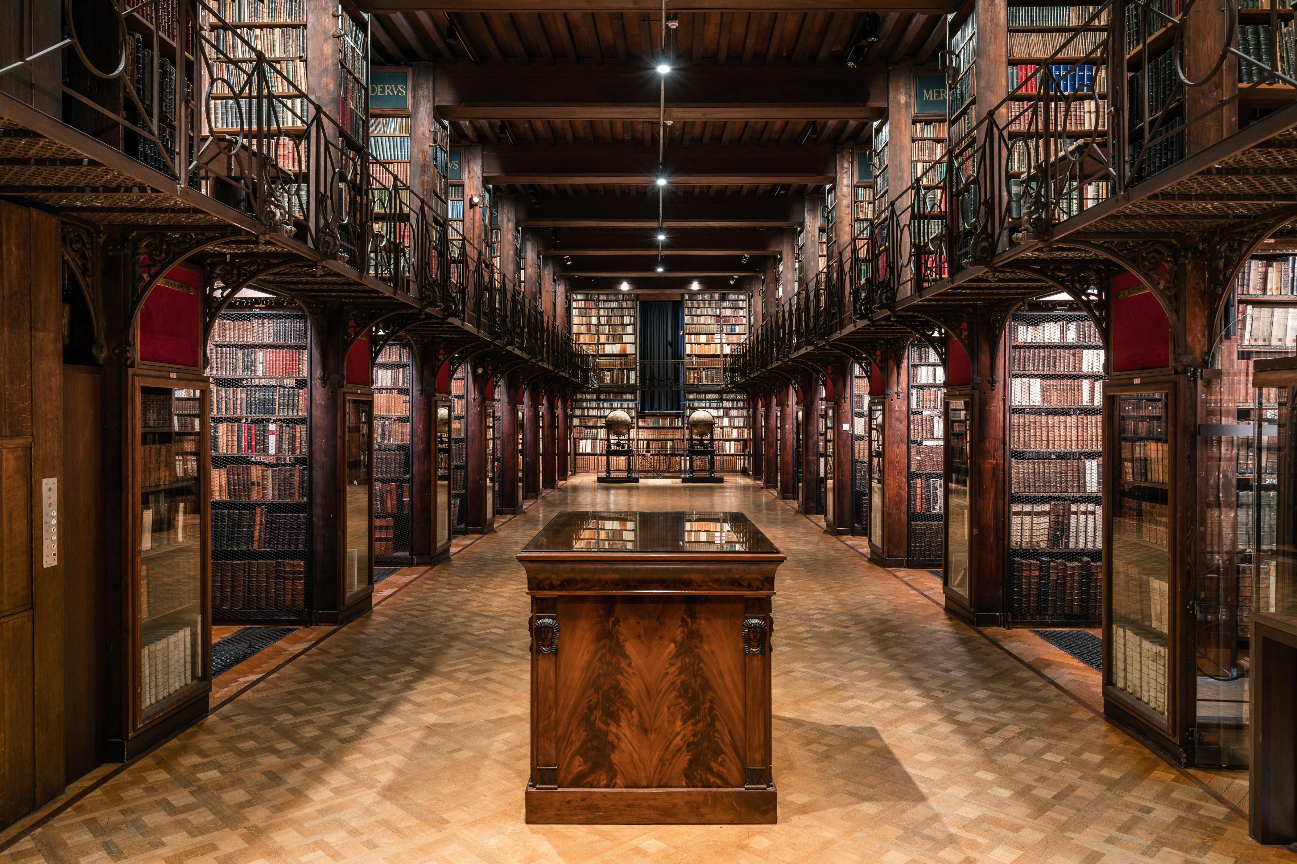 Breed zicht op de De Nottebohmzaal boekenkasten tegen elke muur en enkele vitrinekasten waar oude boeken in liggen. 