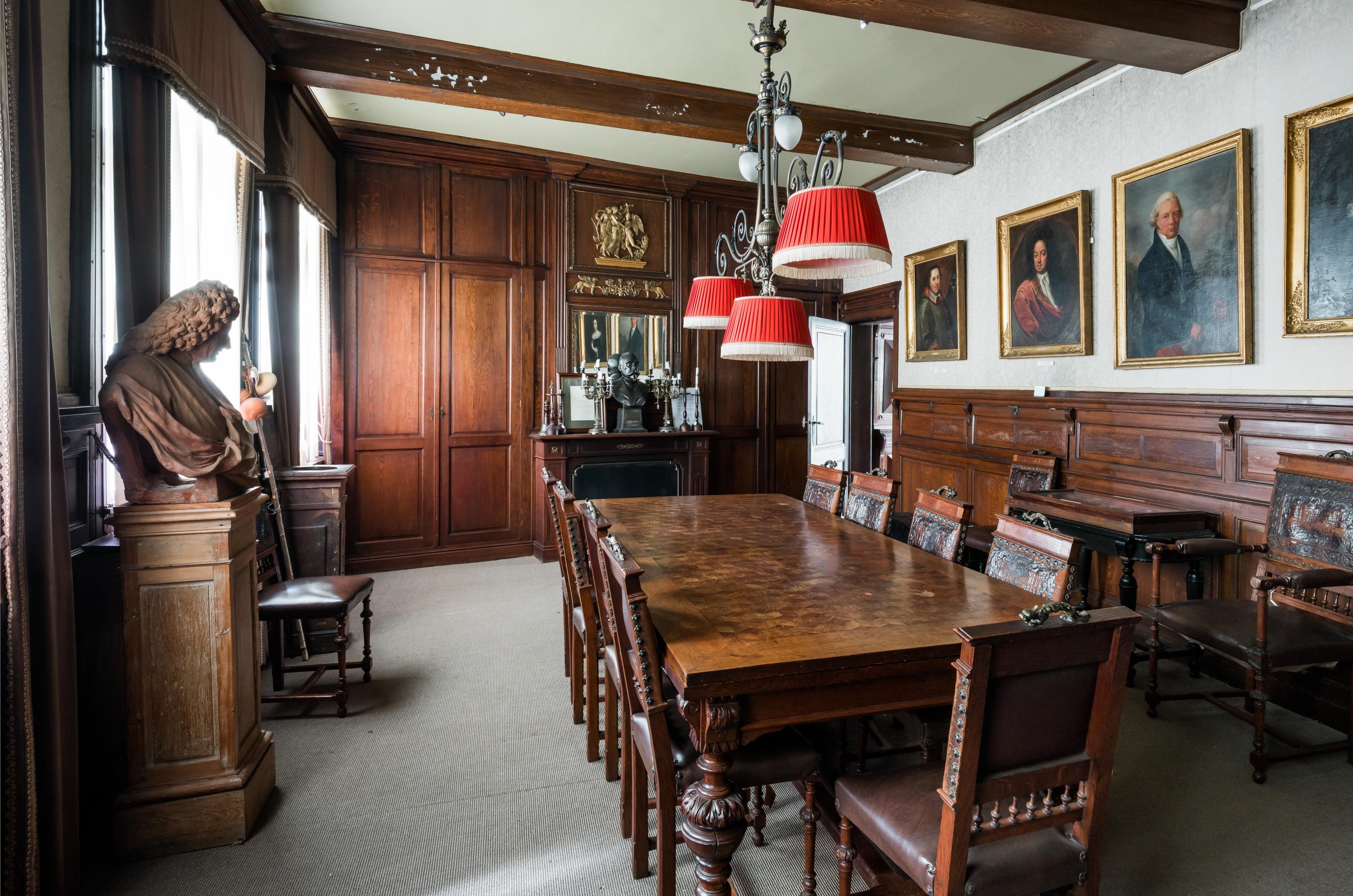 Vergaderzaal met houten lambriserig en houten tafel en stoelen. Schilderijen van mannen sieren de muur.