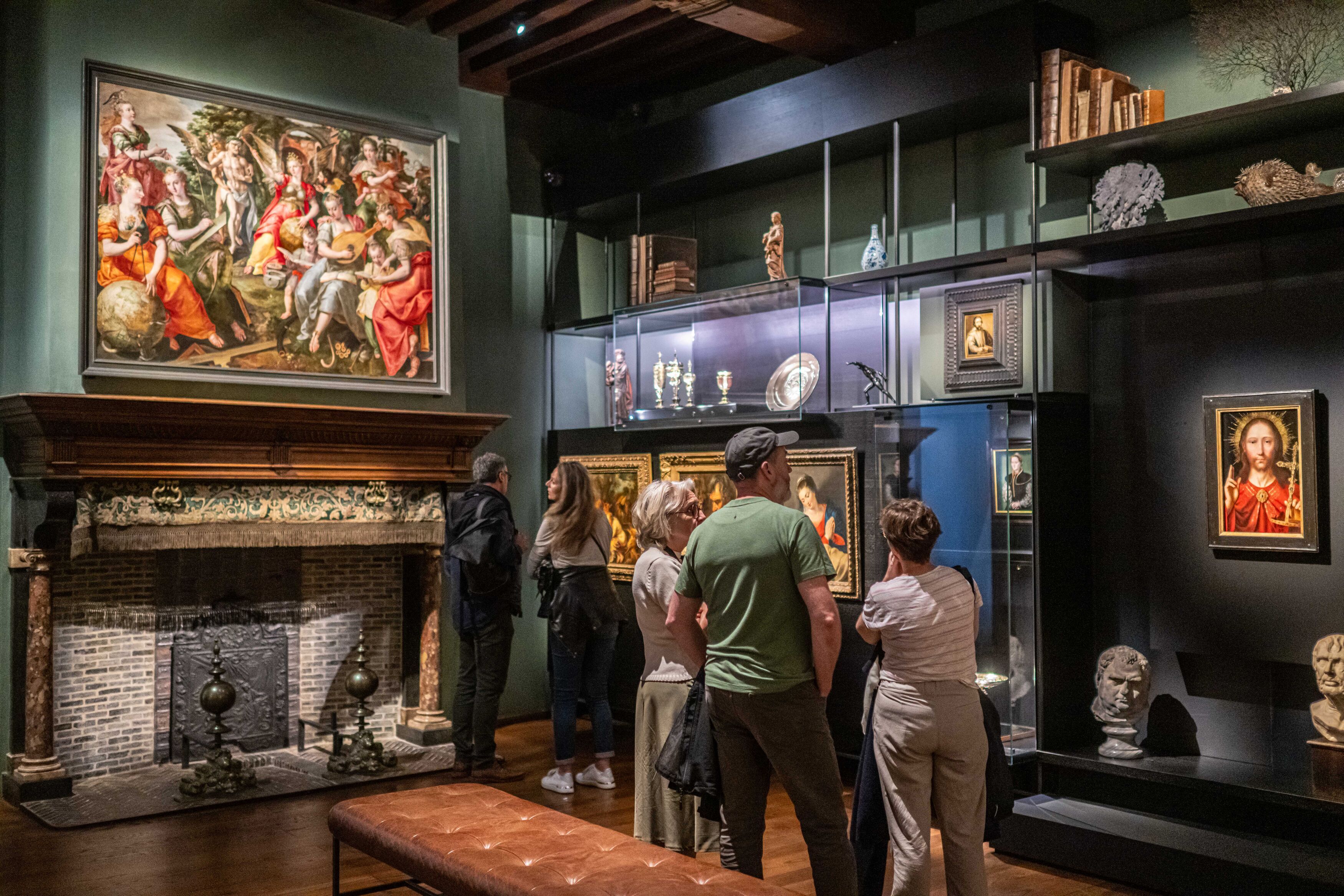 Beeld van binnen het museum. Bezoekers kijken naar schilderijen op de muur en objecten achter glas.