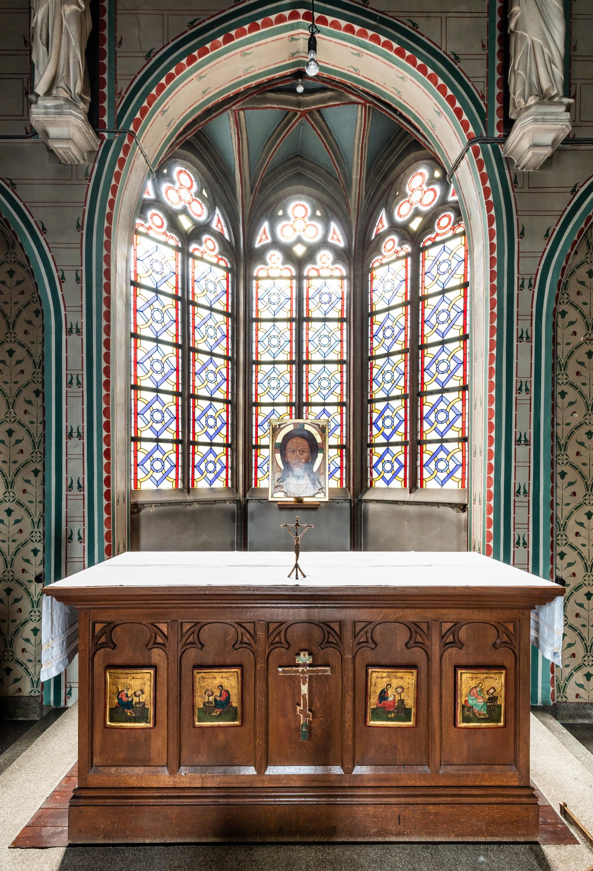 Beeld van een altaar in gotische zaalkerk met op de achtergrond kleurrijke glasramen.