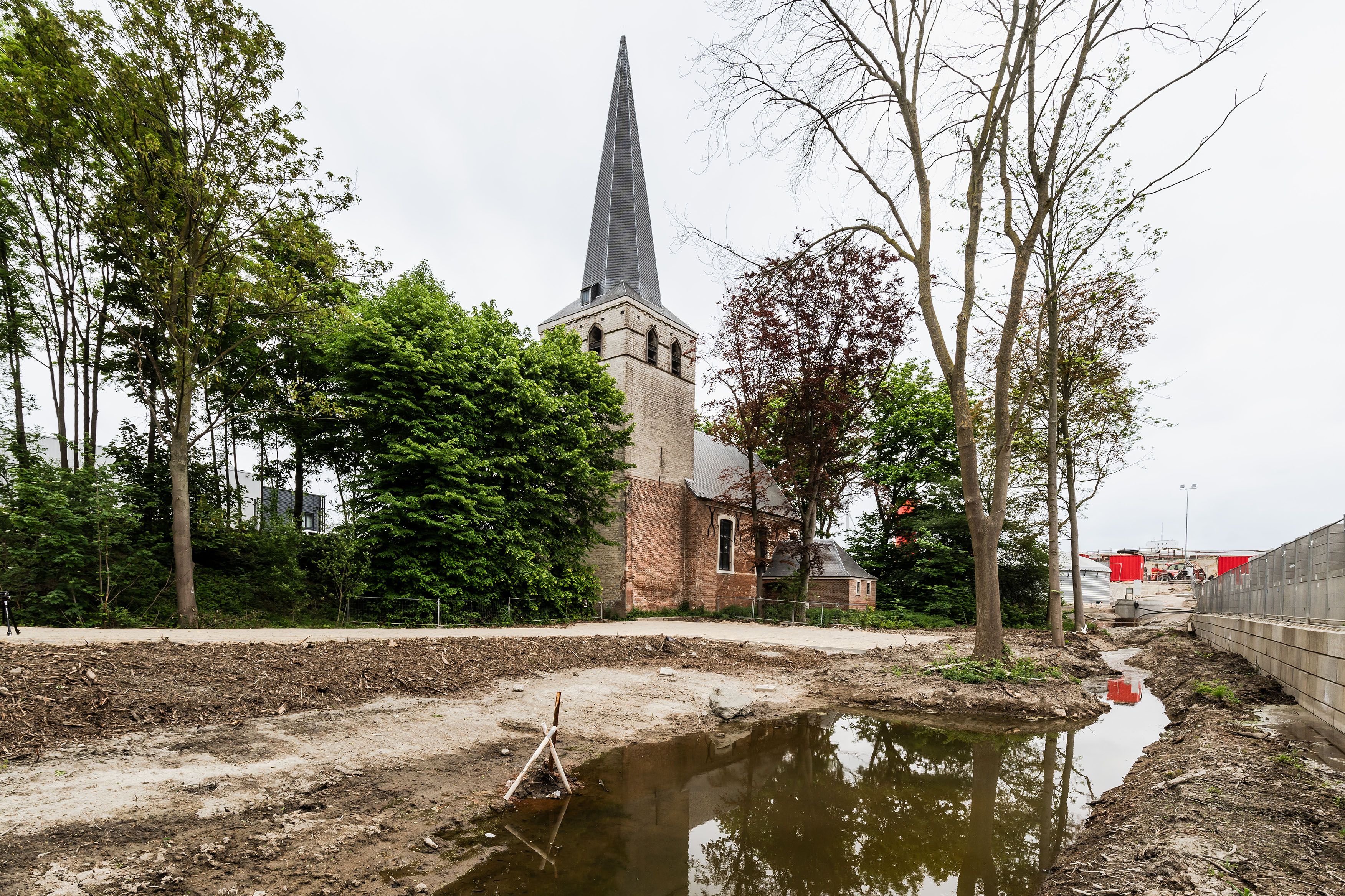 Zandweg met plas en kerktoren met bomen