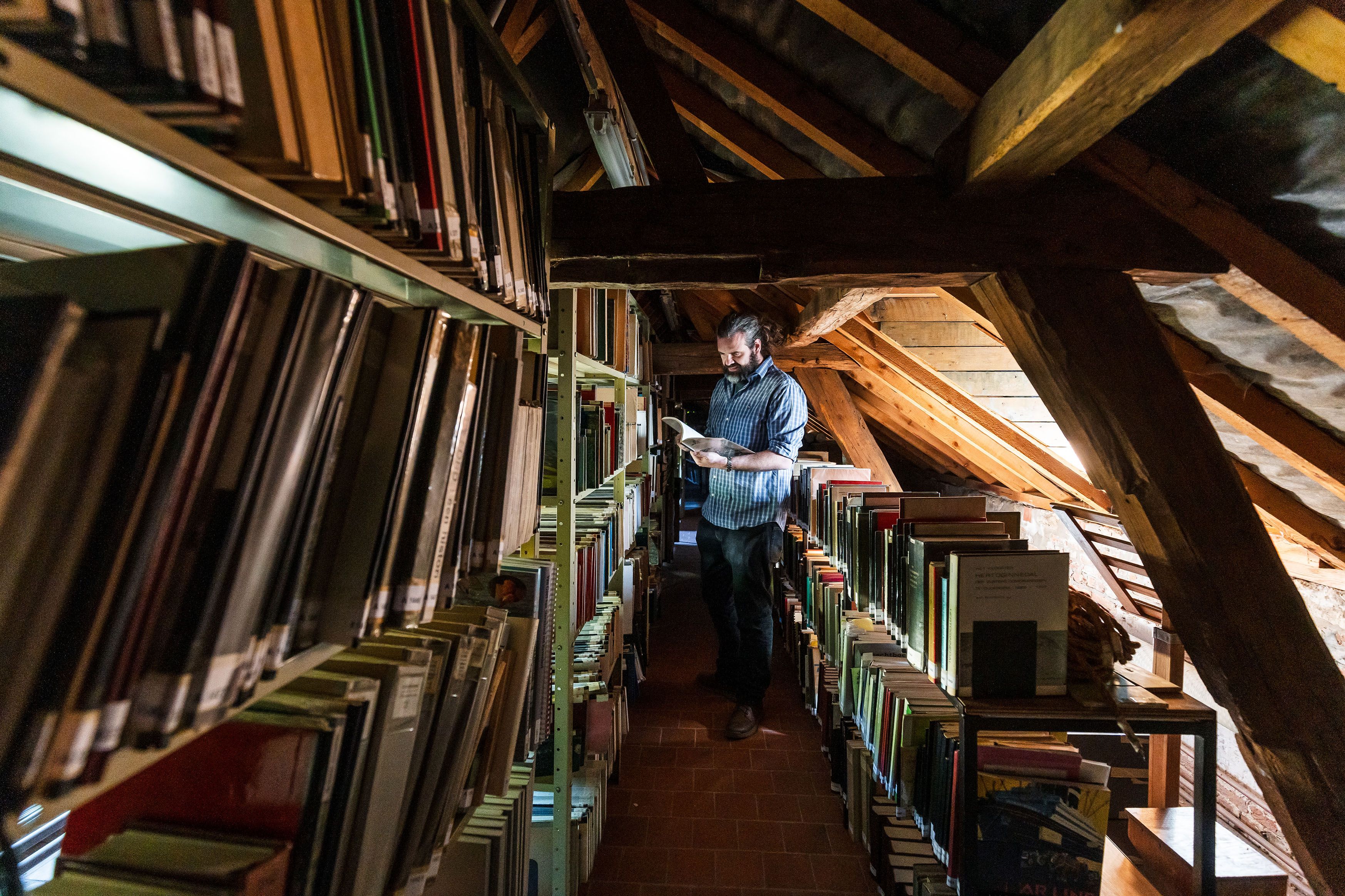 Een vrijwilliger kijkt tussen de boeken van het Documentatiecentrum Antwerpse Noorderpolders. De bibliotheek bevindt zich op een zolder met oude spanten.