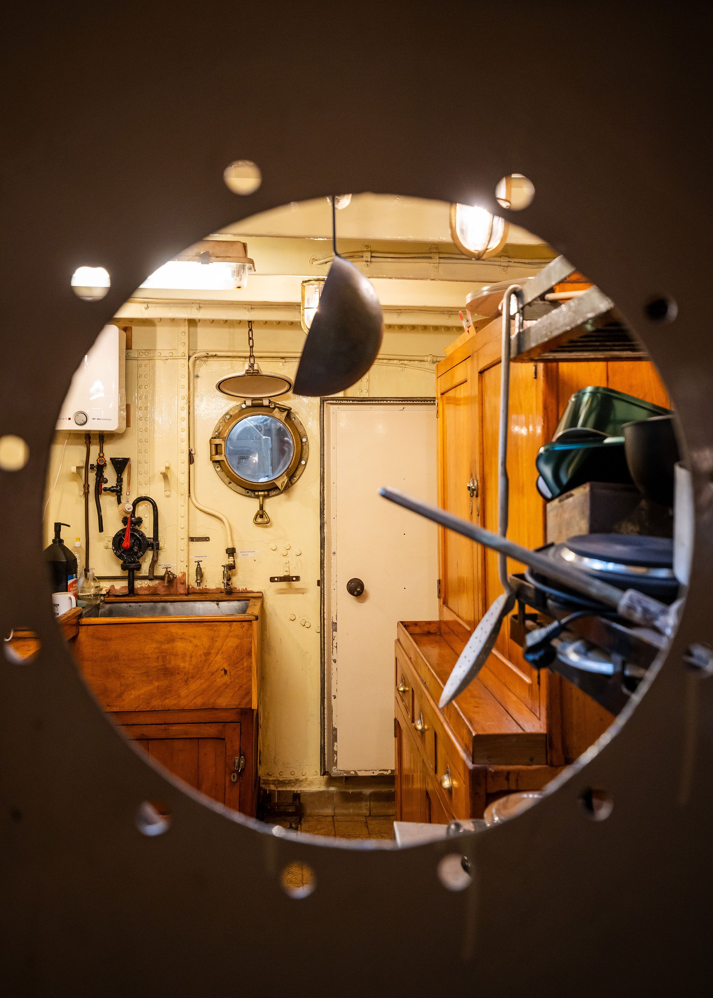 Zicht door een rond raam in een kajuit met houten meubels