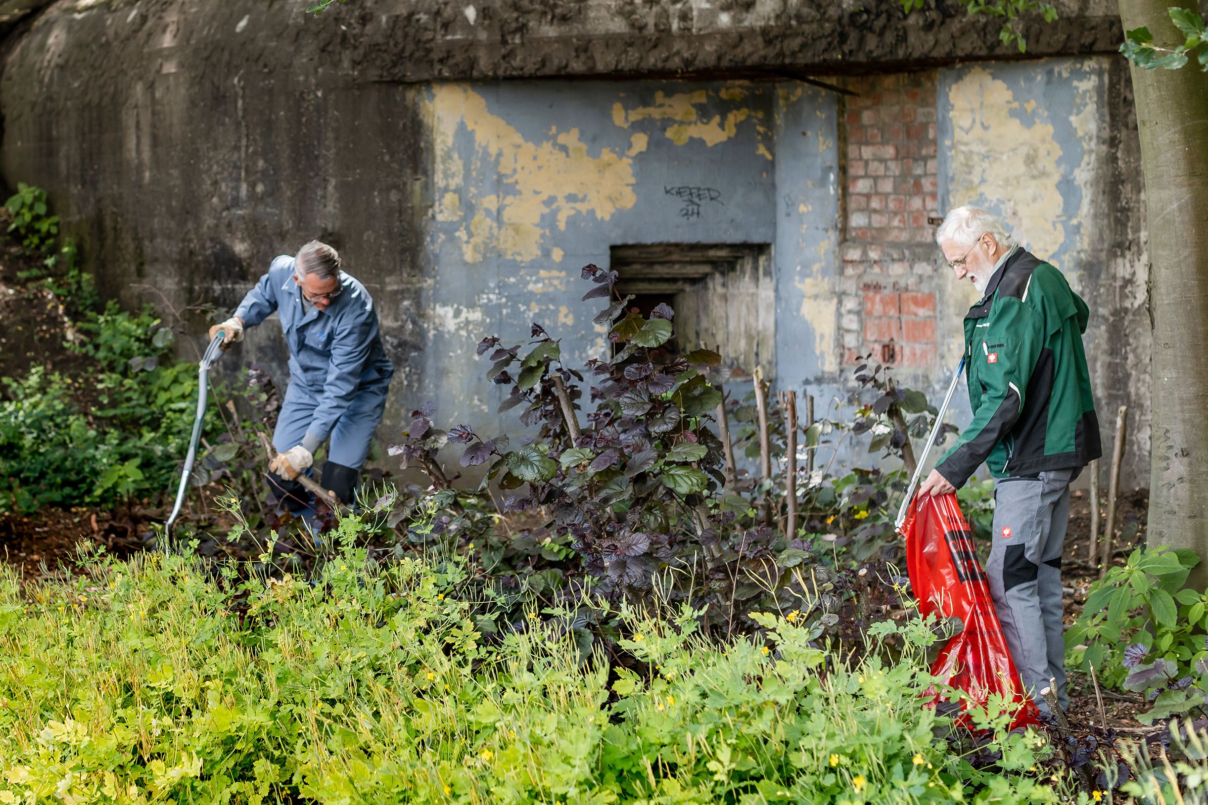 Twee vrijwilligers verzamelen puin rond een van de bunkers in het park Den Brandt.