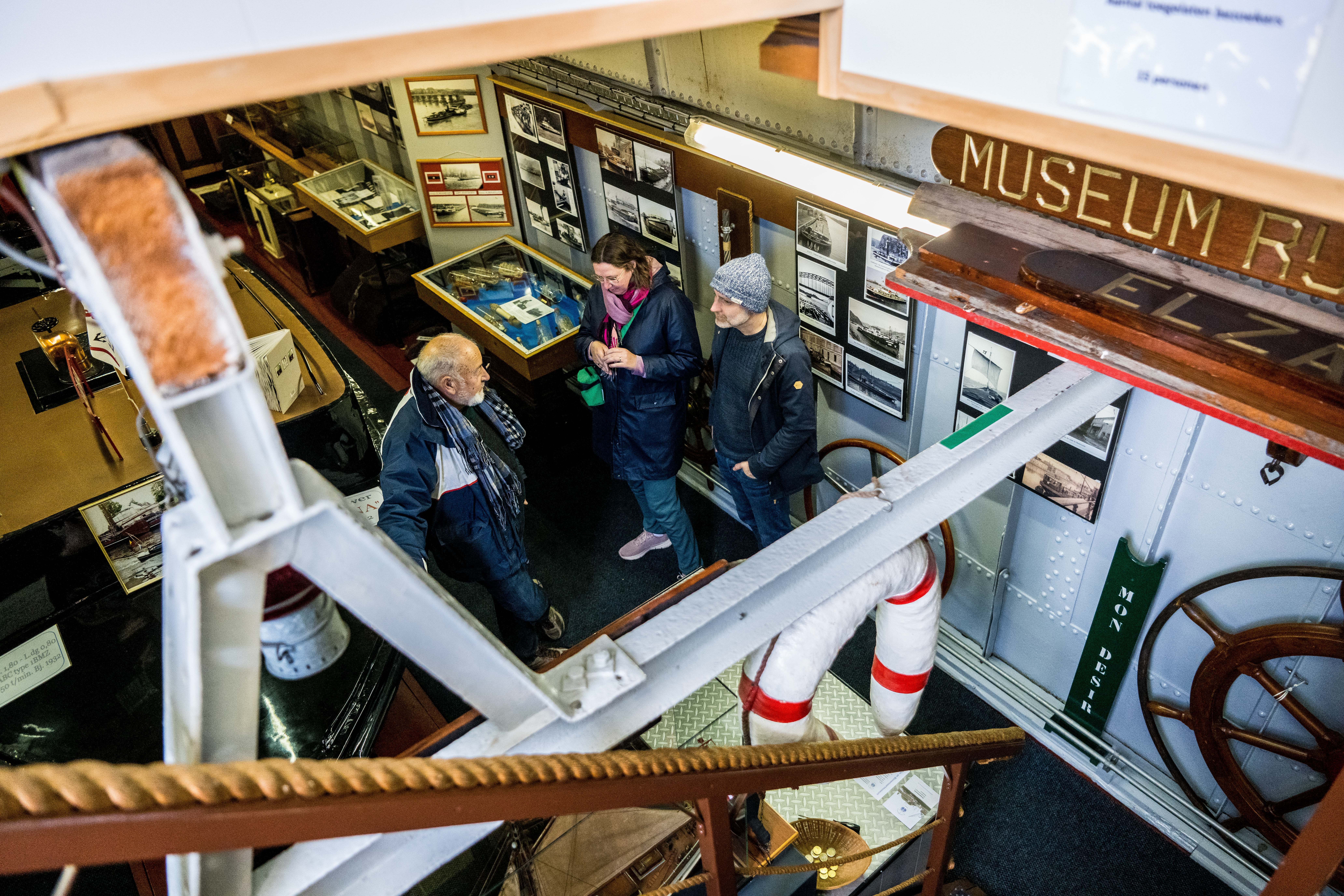 1 man en 2 vrouwen praten met elkaar in een binnenschip dat ingericht is als museum