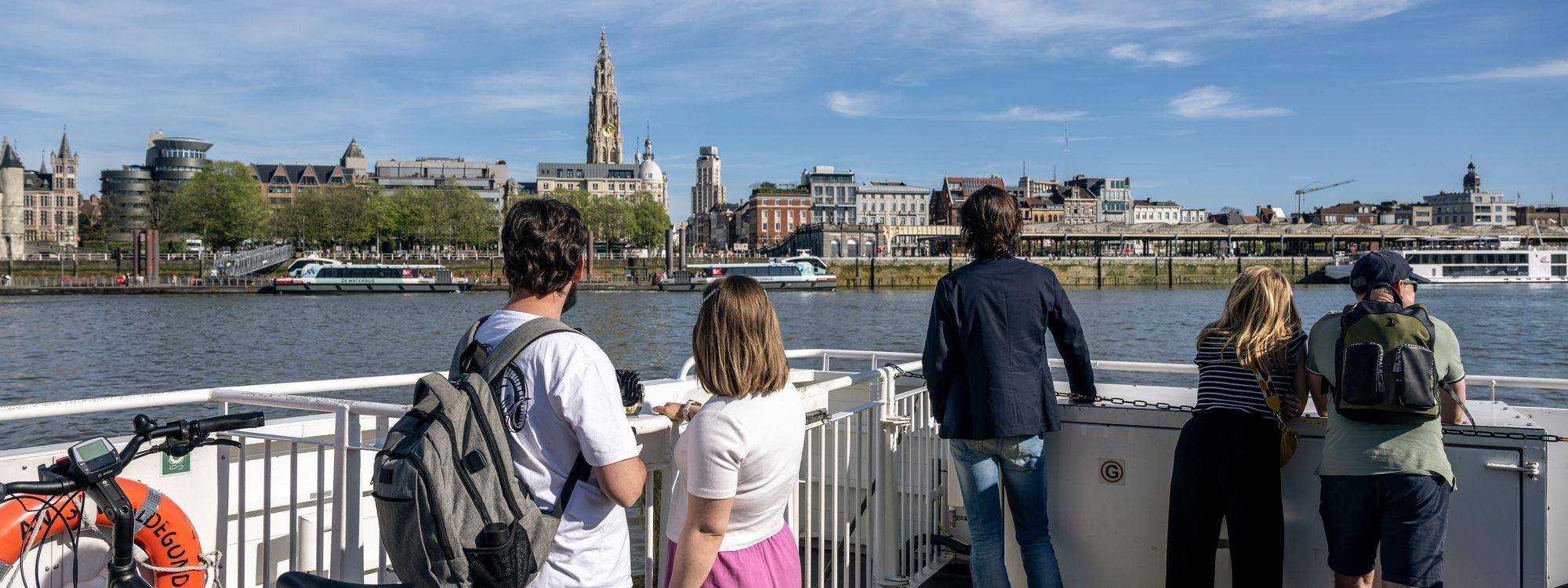 Mensen te voet en met de fiets op de veerboot met zicht op de stad.