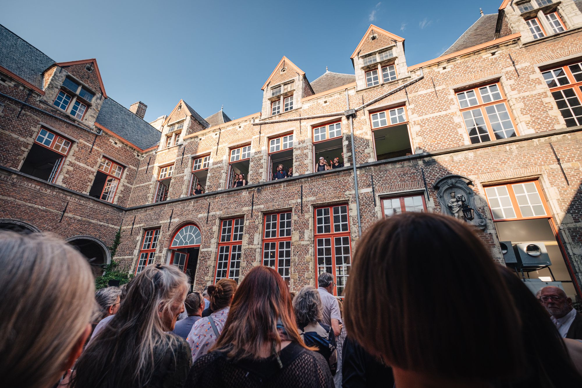 Een groep vrouwen staat voor de binnengevel van het Maagdenhuis. Een rode bakstenen gevel met rode ramen.