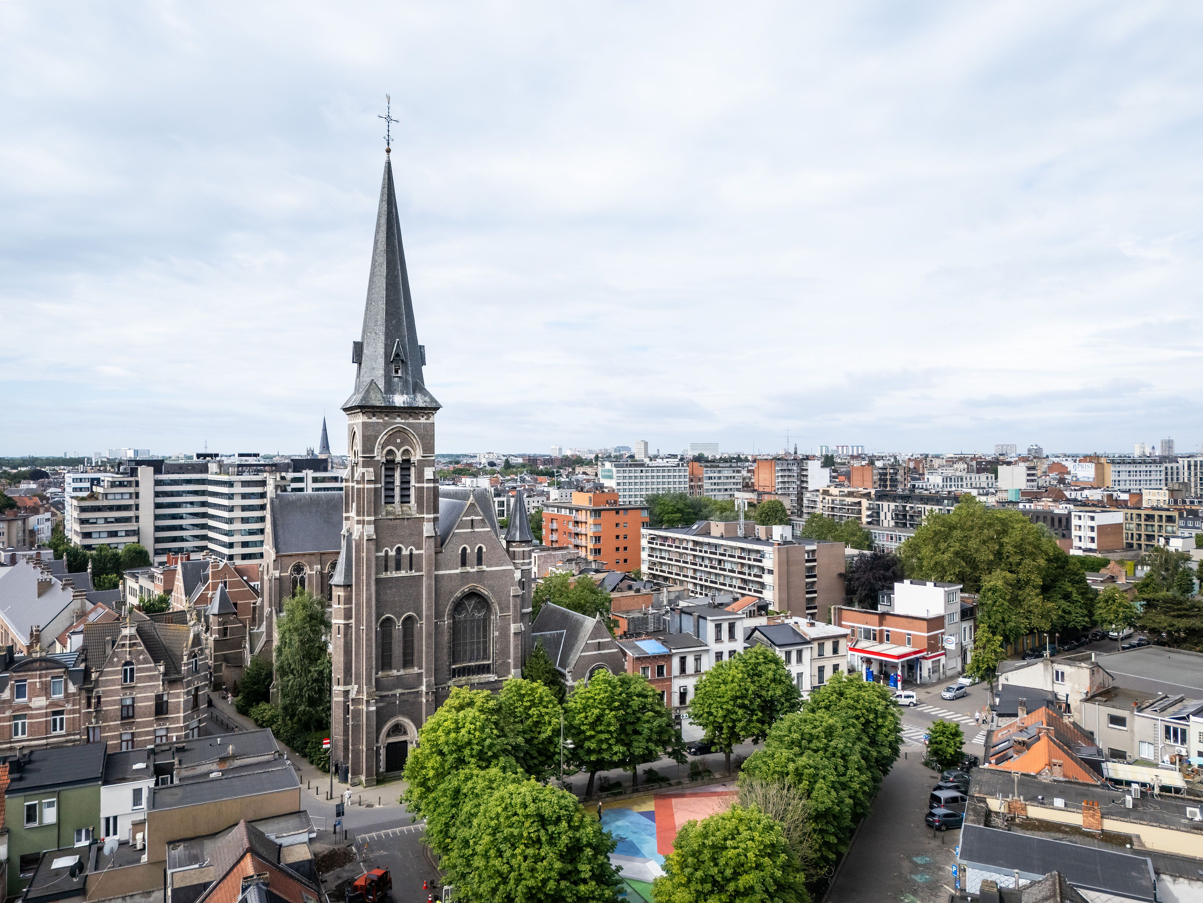 Luchtfoto met zicht op de Heilige Familiekerk, een pleintje met bomen en veel appartementsgebouwen