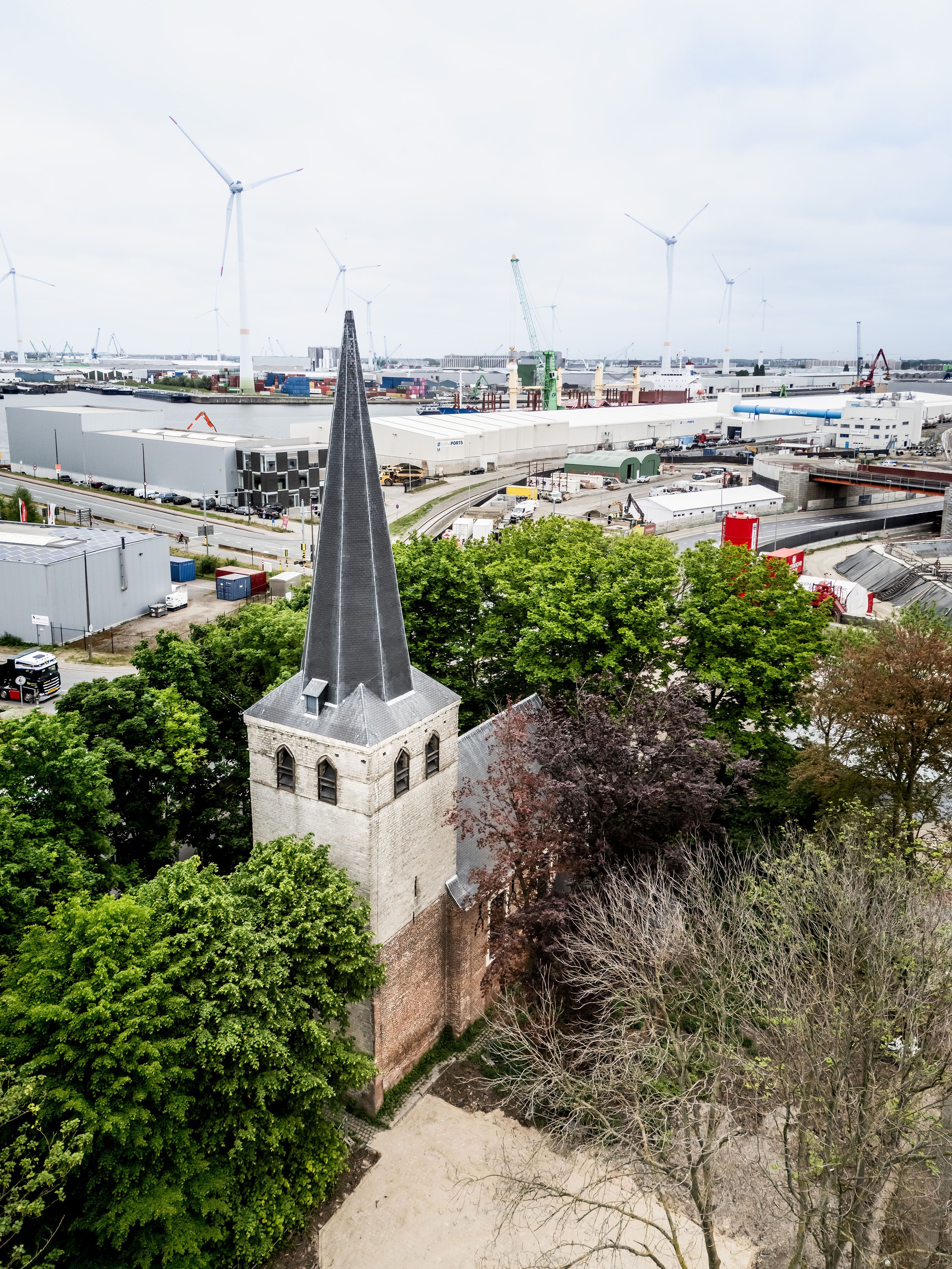 Lager gelegen kerktoren, omringd door bomen en door de haven