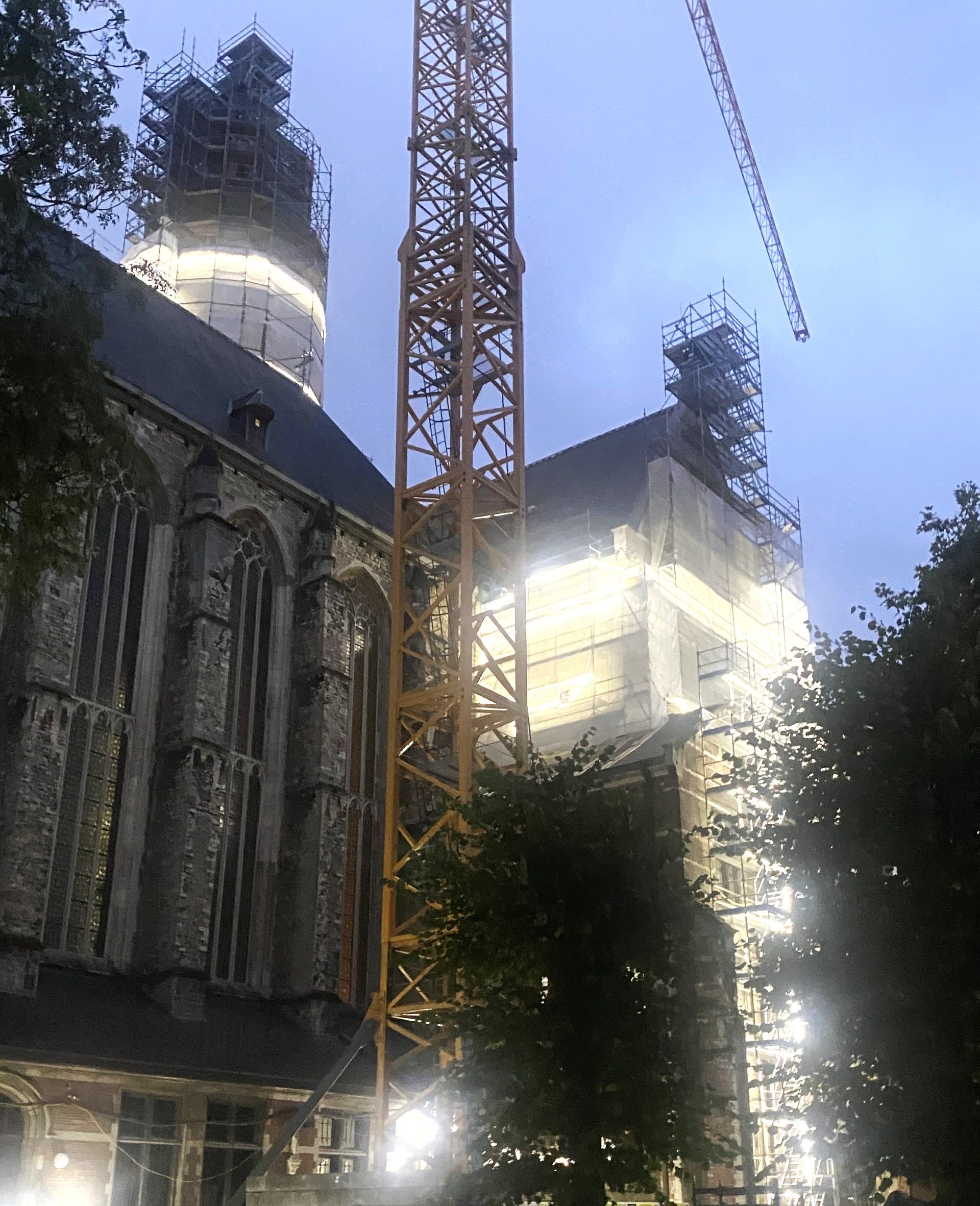 Deel van de buitengevel van de Sint-Pauluskerk is verlicht. Voor de kerk staat een kraan. Het schemert.