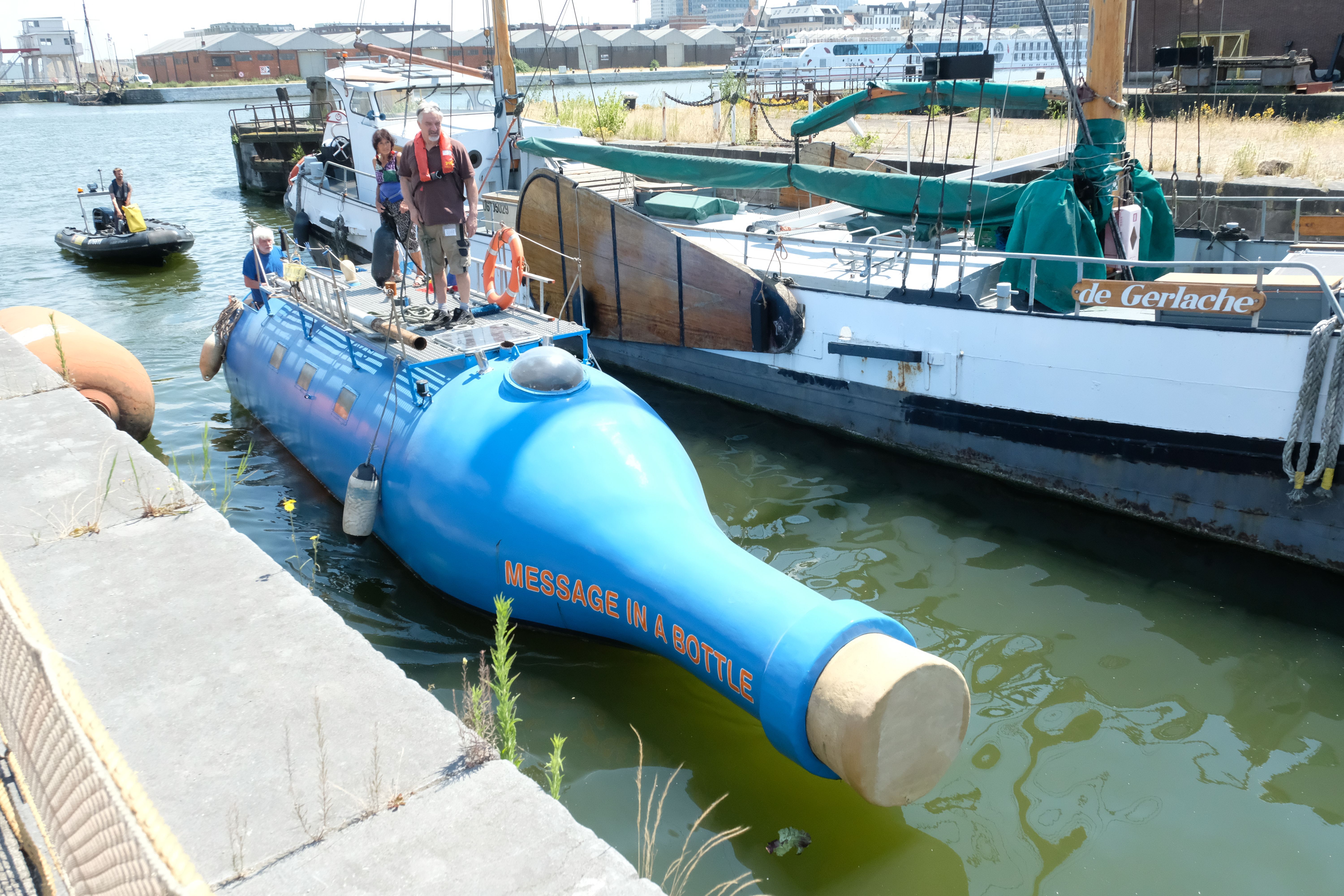 Man en vrouw staan op een grote felblauwe fles die op het water vaart