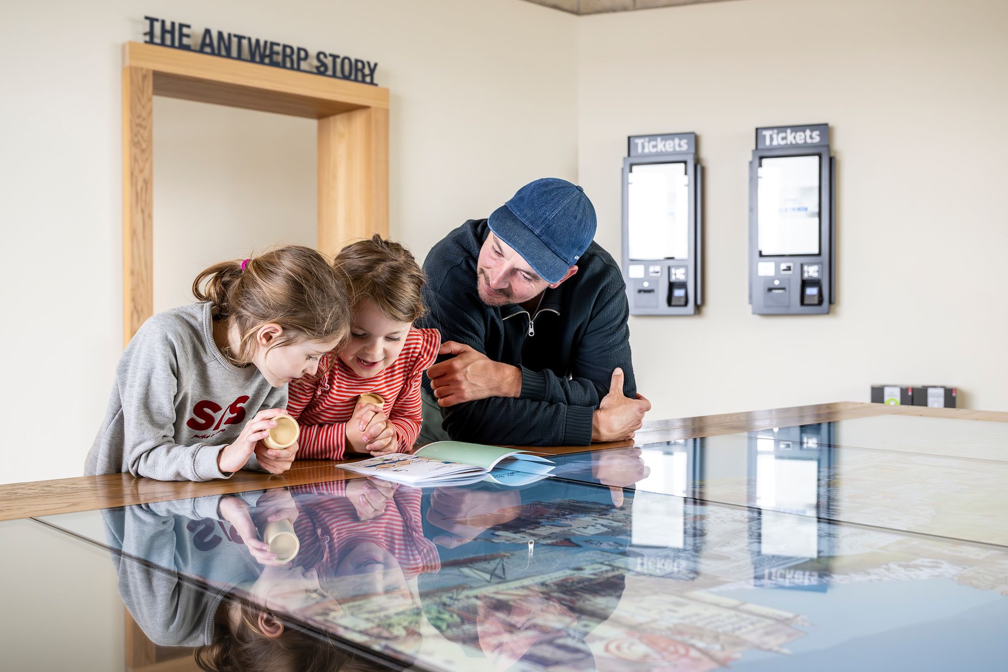 Een man en twee kinderen bekijken de tentoonstelling The Antwerp Story