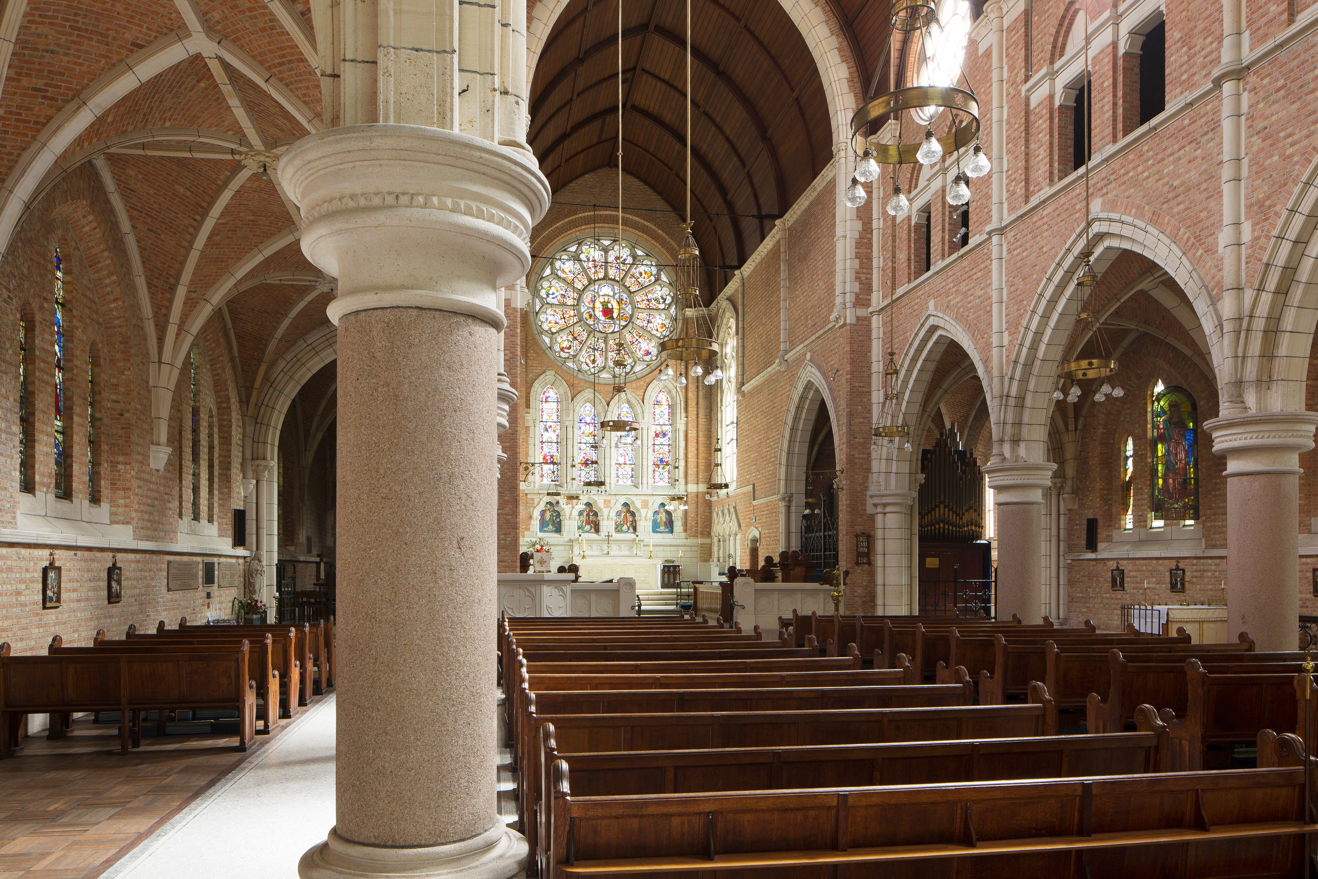 Interieur Sint-Bonifaciuskerk met lichte zuilen en rolde bakstenen muren, lange houten banken.