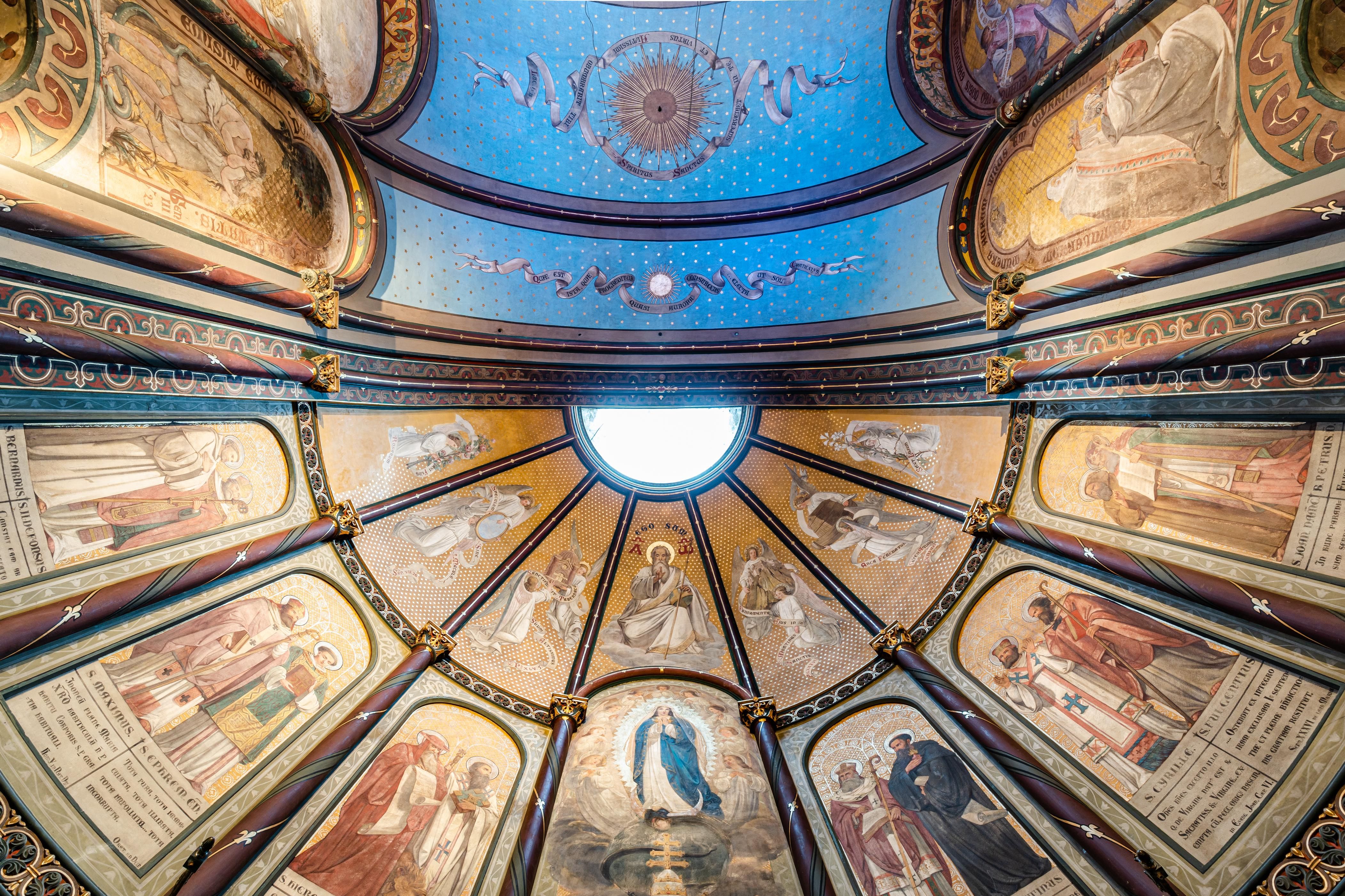 Zicht op helderblauw plafond met religieuze schilderijen op de muren. 
