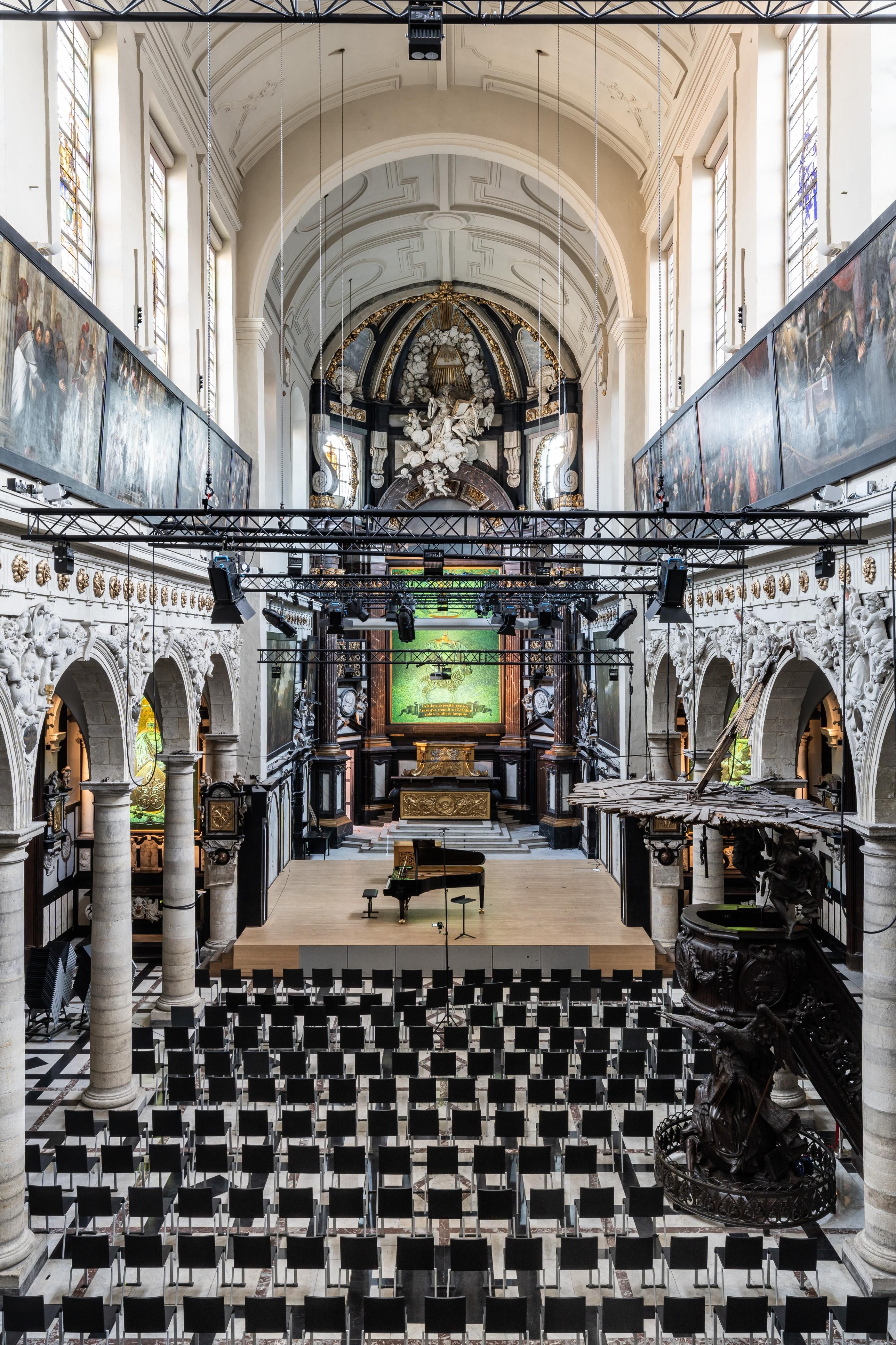 Vooraanzicht van het podium met stoel ervoor in een ruimte die barok uitstraalt. Aan het plafond hangen spots om lichttechniek toe te passen.