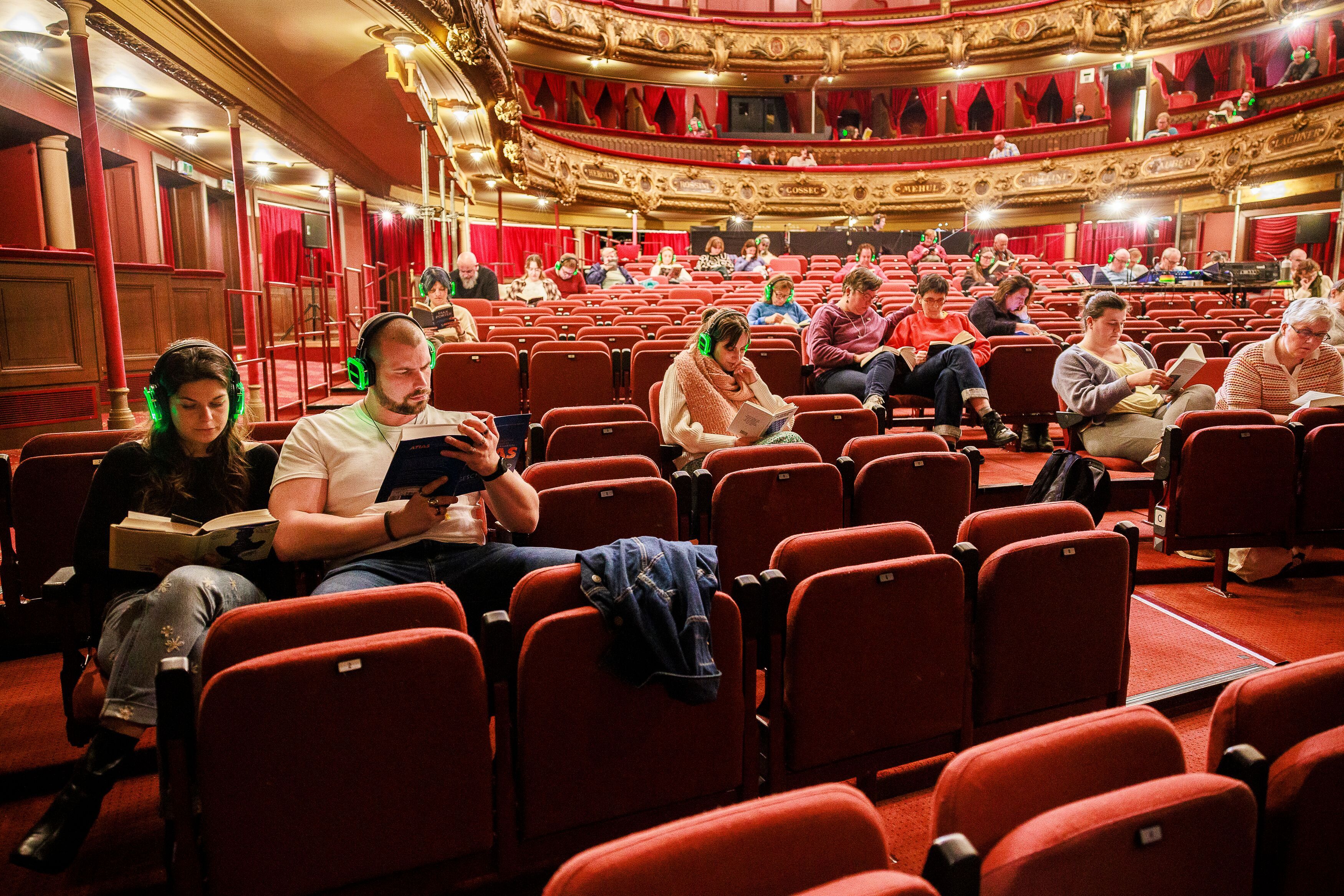 In de Bourlaschouwburg zitten her en der mensen een boek te lezen met een koptelefoon op hun hoofd.