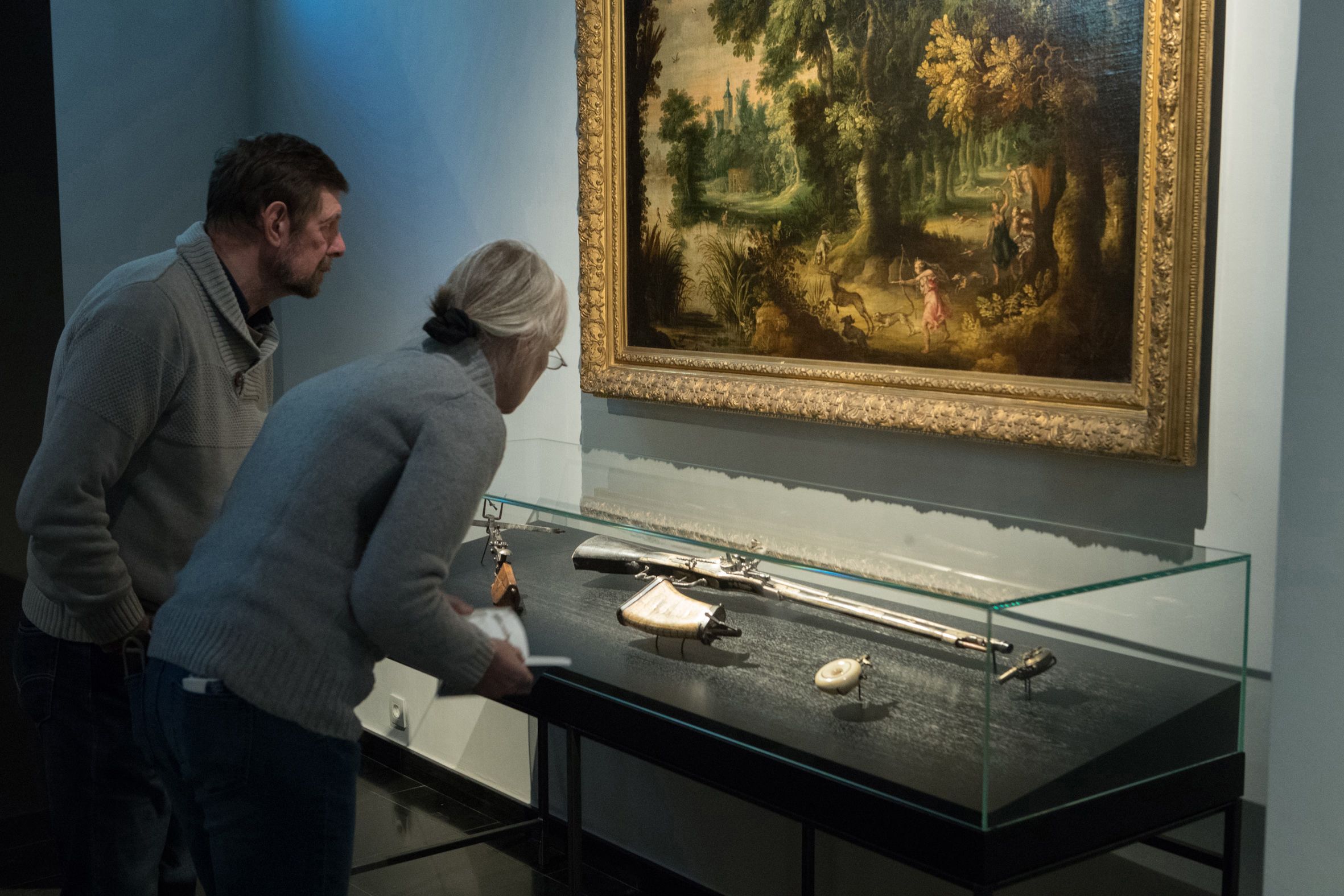 Tentoonstelling in Snijders&Rockoxmuseum. Een donker verlichte ruimte kijken bezoekers naar een vitrinekast met objecten.