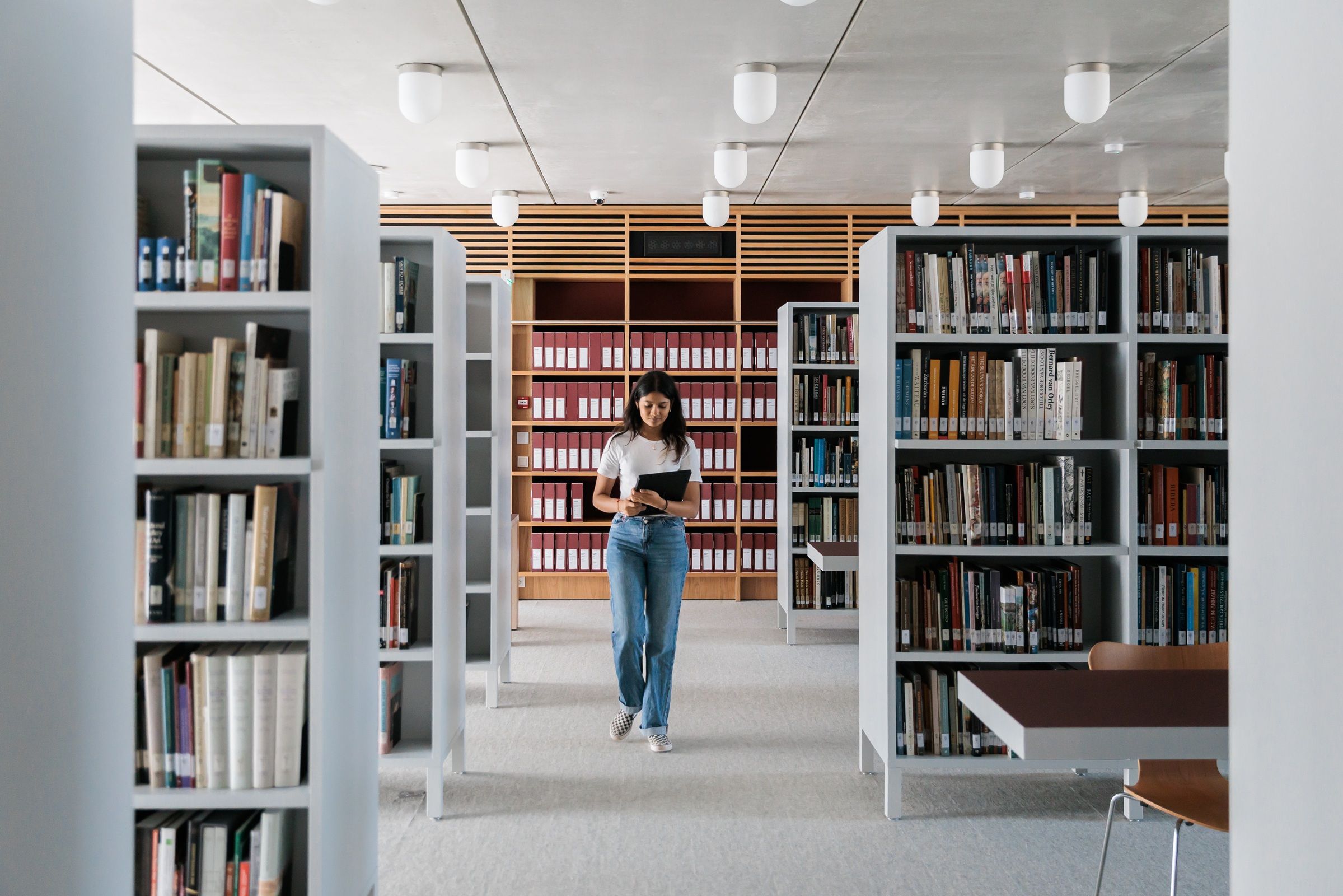 Meisje wandelt met een opengeslagen boek tussen boekenrekken