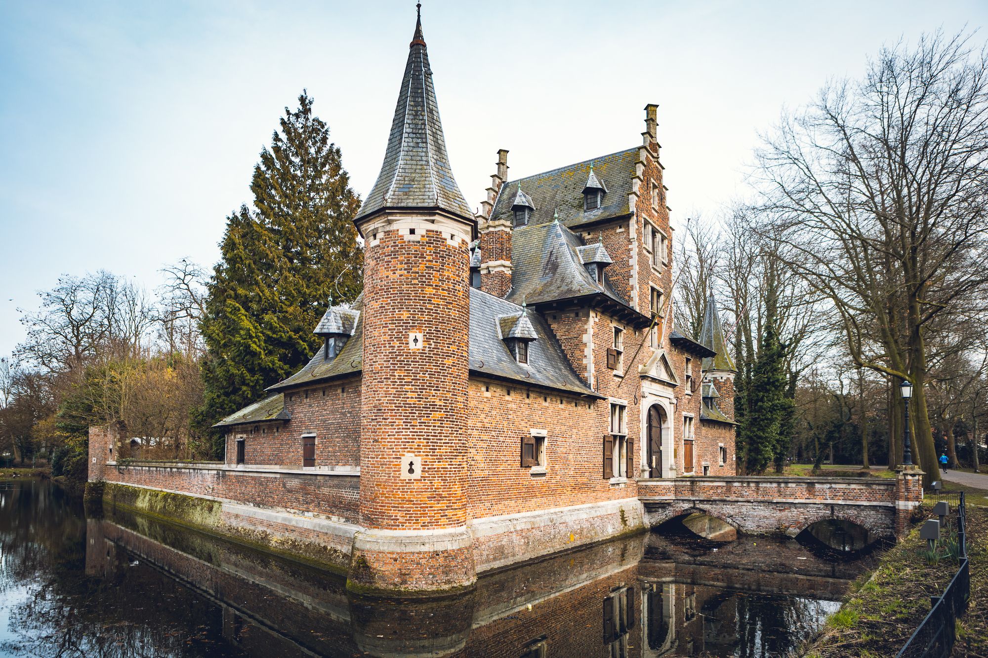Kasteeltje met hoektoren in rode baksteen, zwarte leien daken en gracht errond.