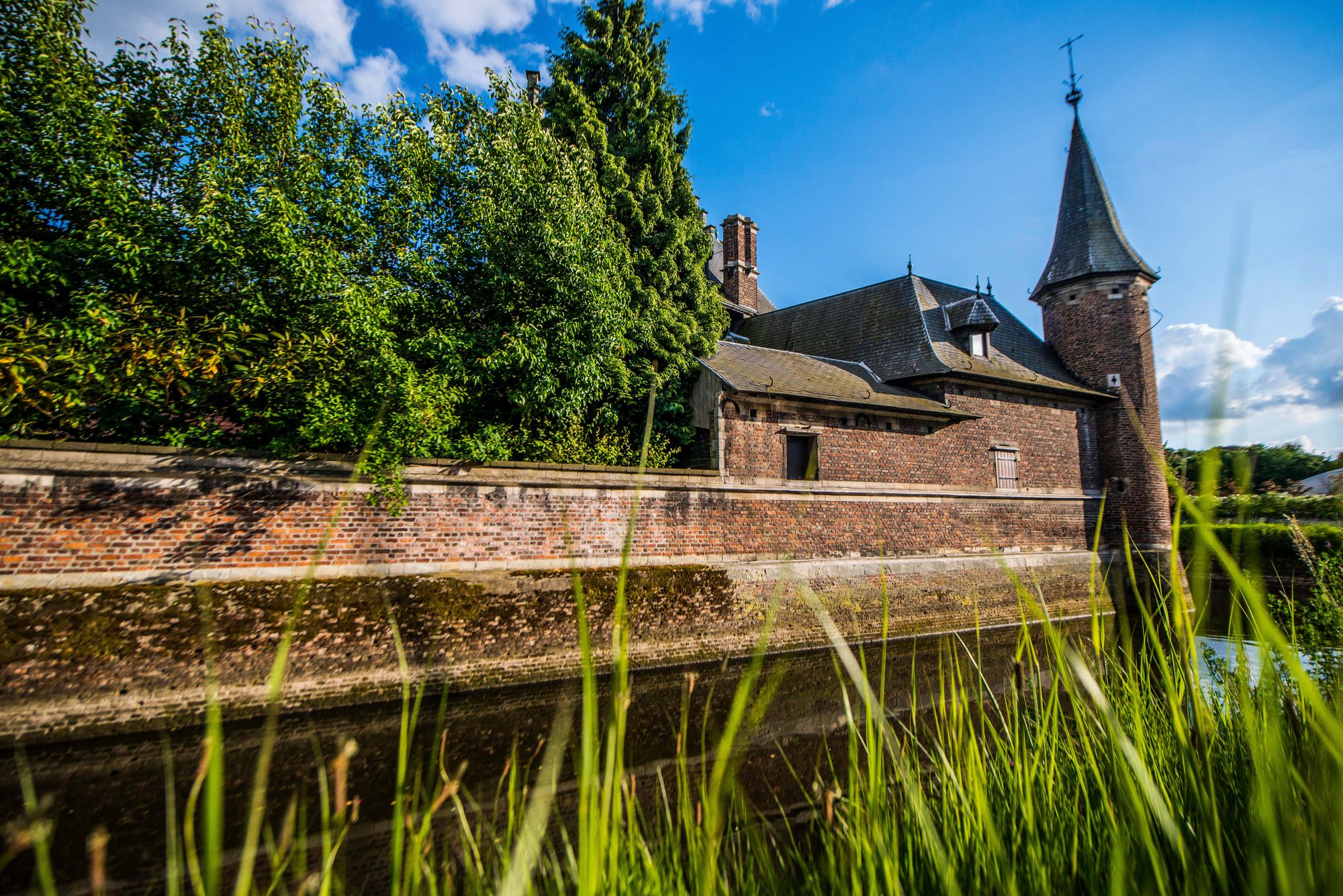 Rode bakstenen muur rond het Hofke van Roosendael met zicht op hoog gras en bomen achter de muur.
