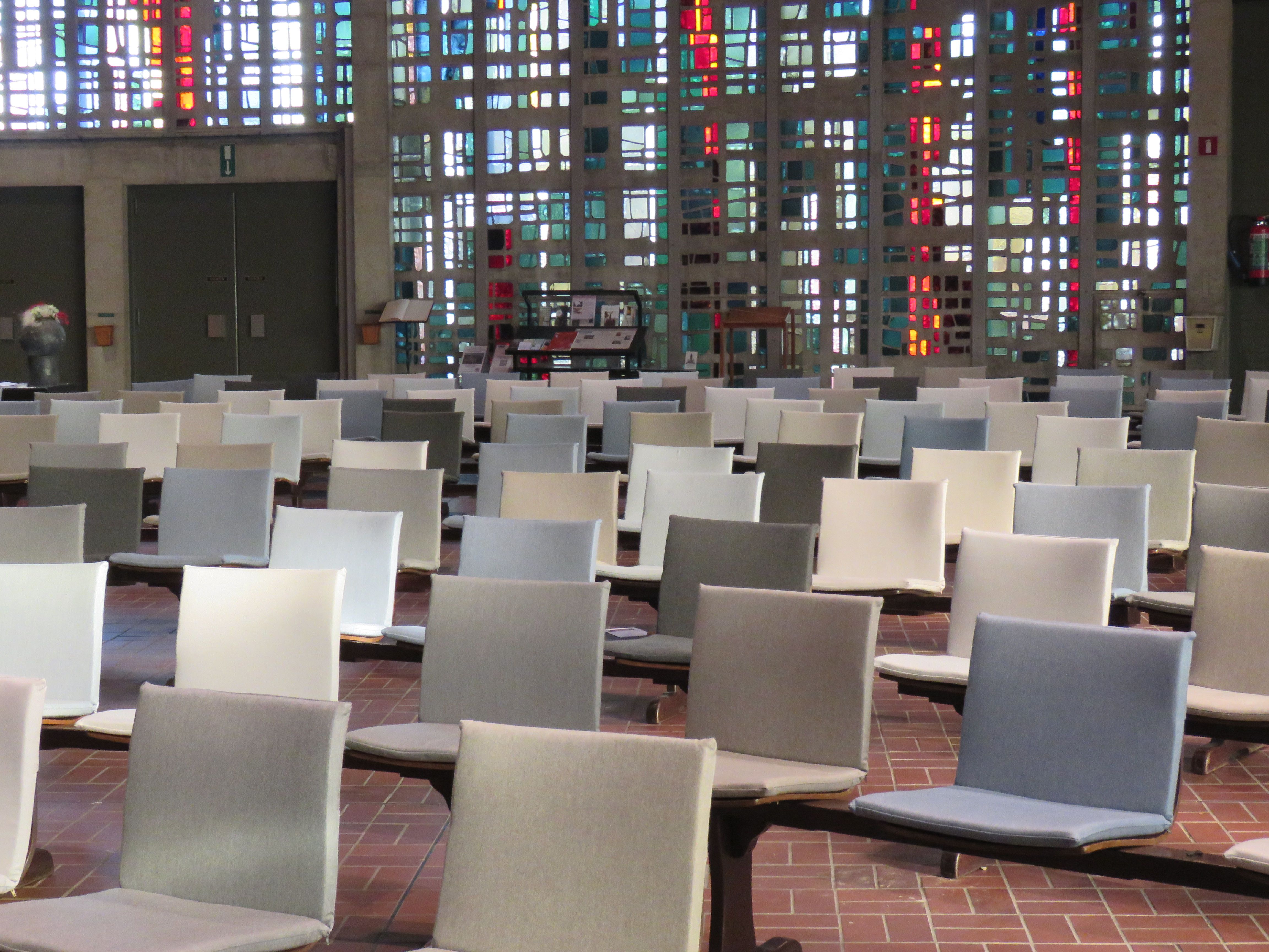 Binnenbeeld van de kerk met stoeltjes in lichte tinten en het glas-in-betonraam