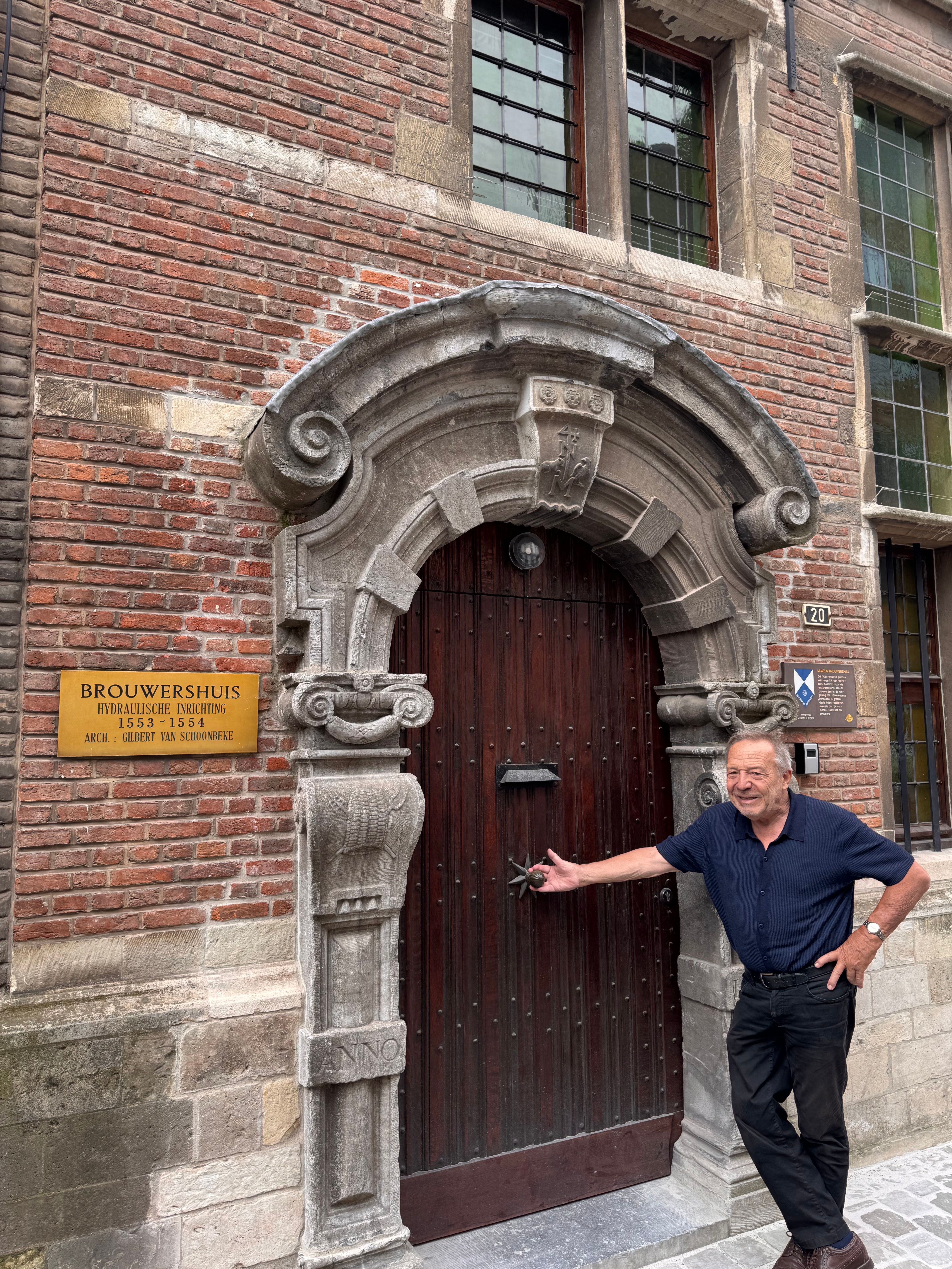 Man van middelbare leeftijd leunt met rechterhand tegen houten poort