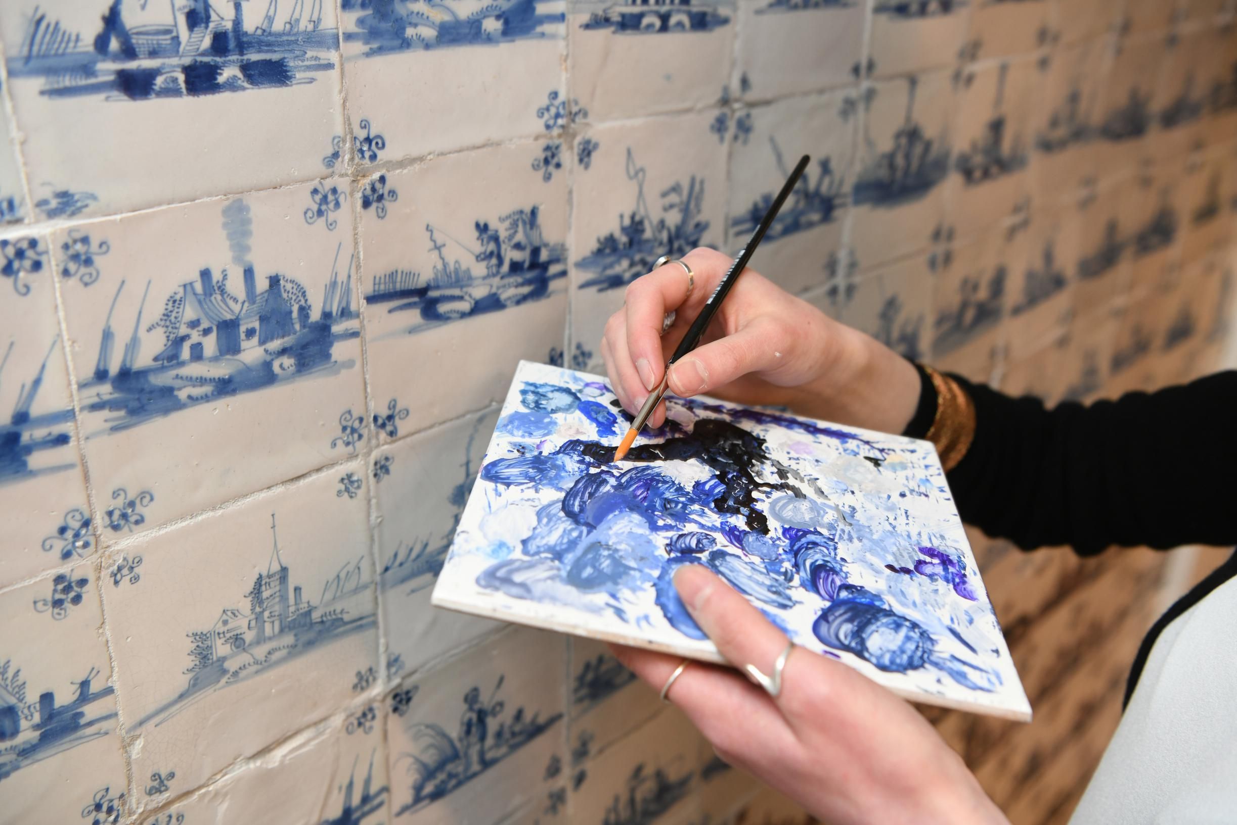 Tegen een muur in de tegelkamer wordt een palet getoond met de verschillende tinten blauw die gebruikt worden voor het retoucheren van de blauwwitte tegels.