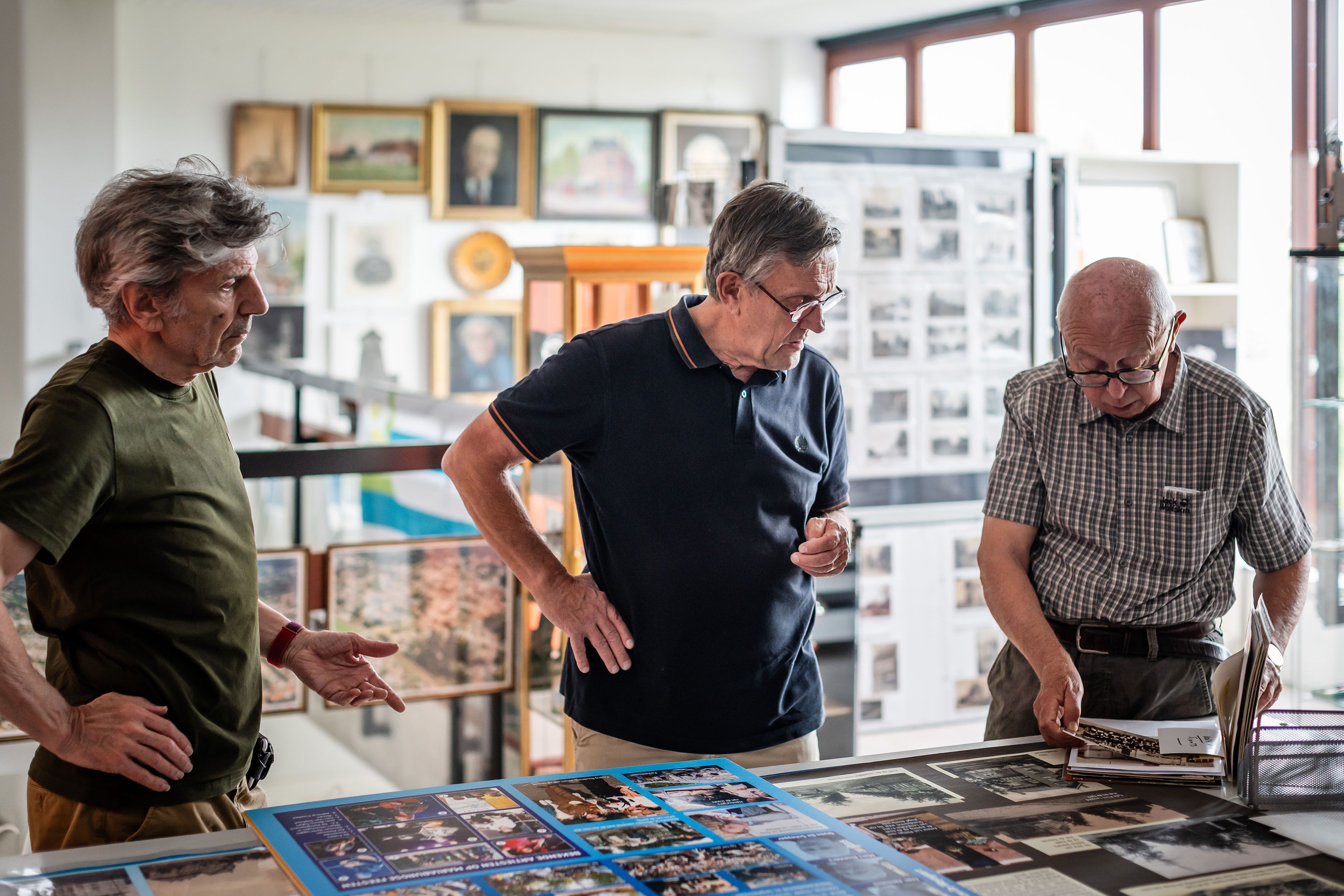 Drie mannelijke vrijwilligers staan over een tafel gebogen. Ze kijken naar oude foto's in het wijkcentrum Sint-Mariaburg.