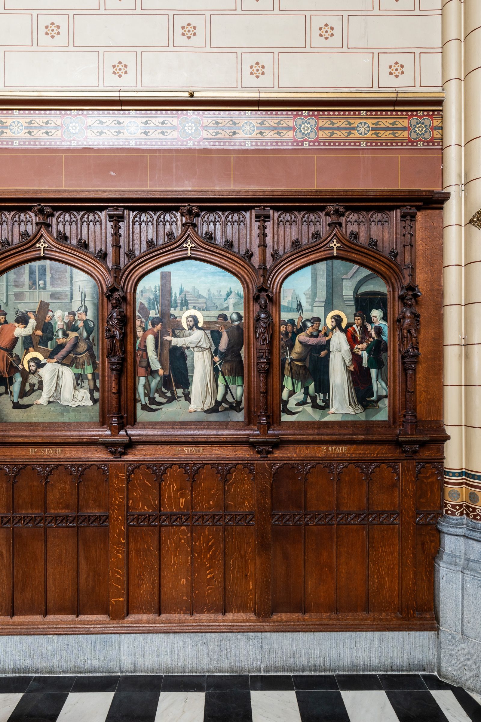 Houten lambrisering met erboven een witte muur met baksteenimitatie. De nissen van de lambrisering zijn opgevuld met schilderijen met religieuze taferelen.