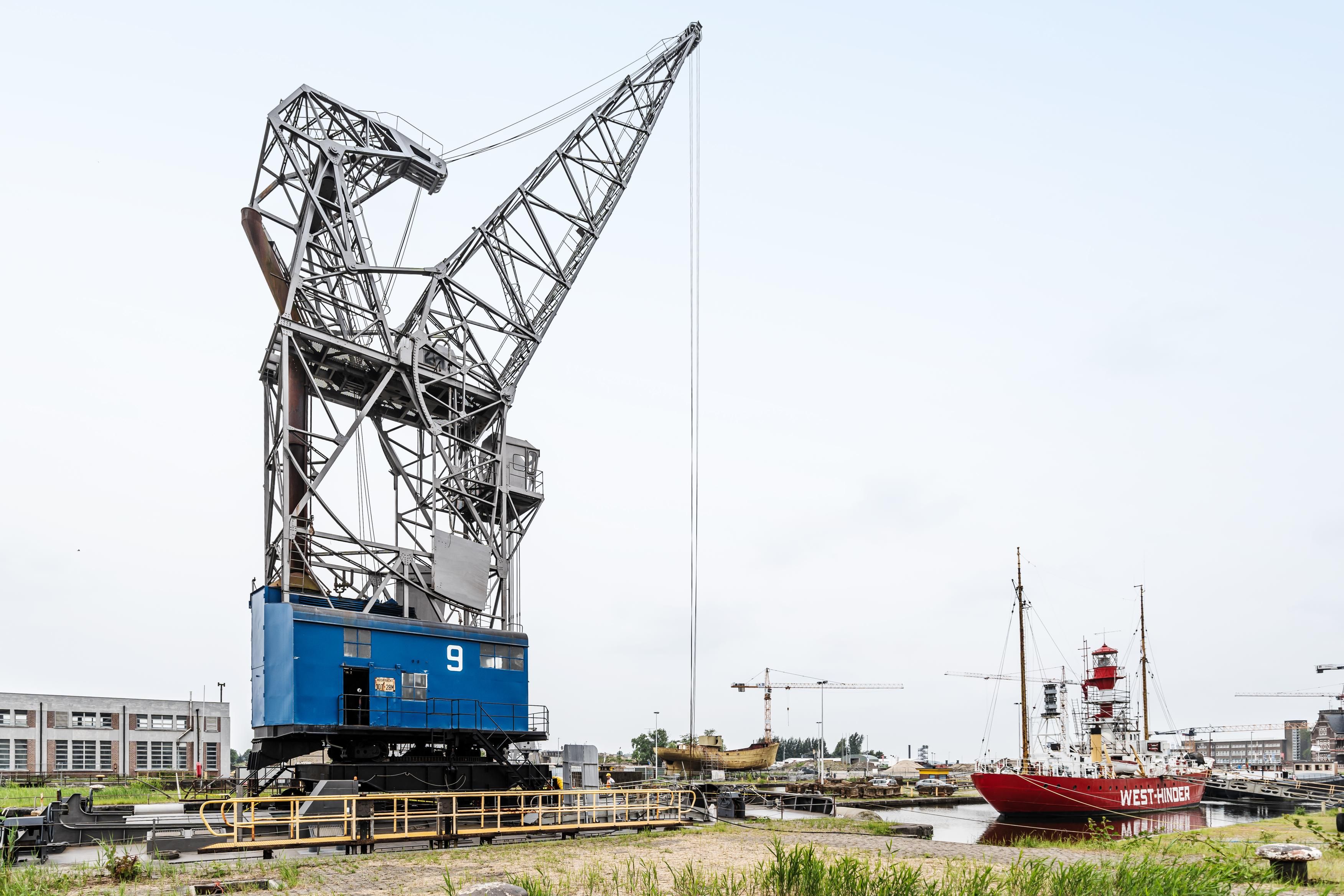 Grote kraan met daarnaast een rood schip in een dok