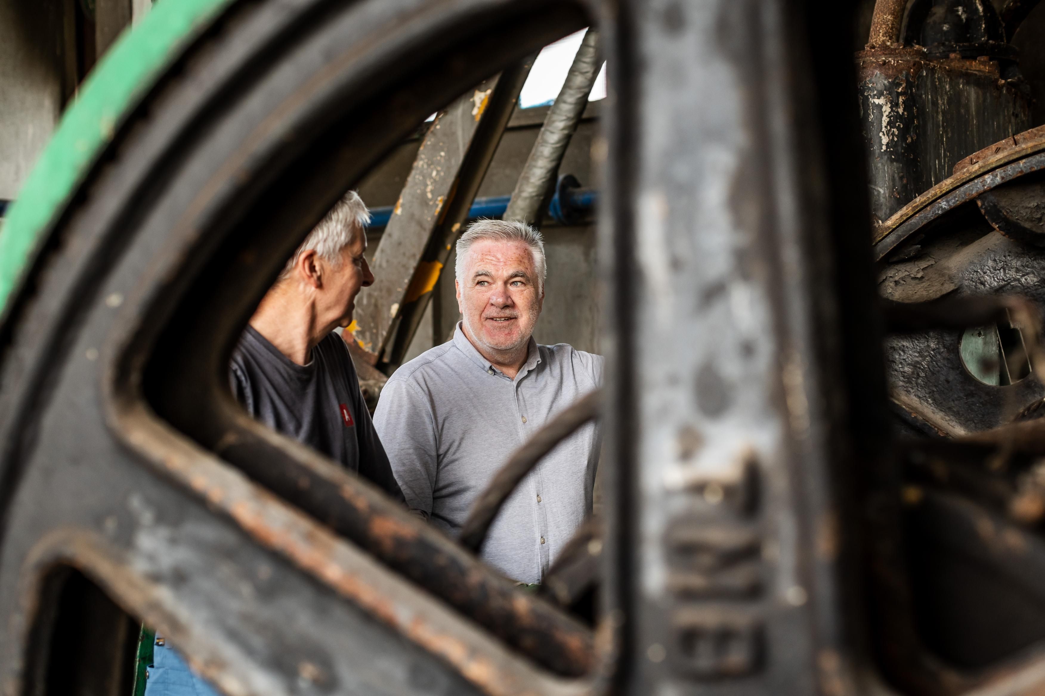 Je kijkt door een metalen wiel naar 2 pratende mannen