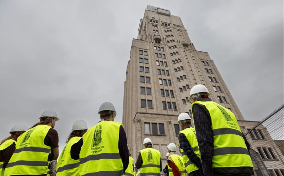 Bezoekers in fluohesje kijken buiten naar de Boerentoren in kikkerperspectief.