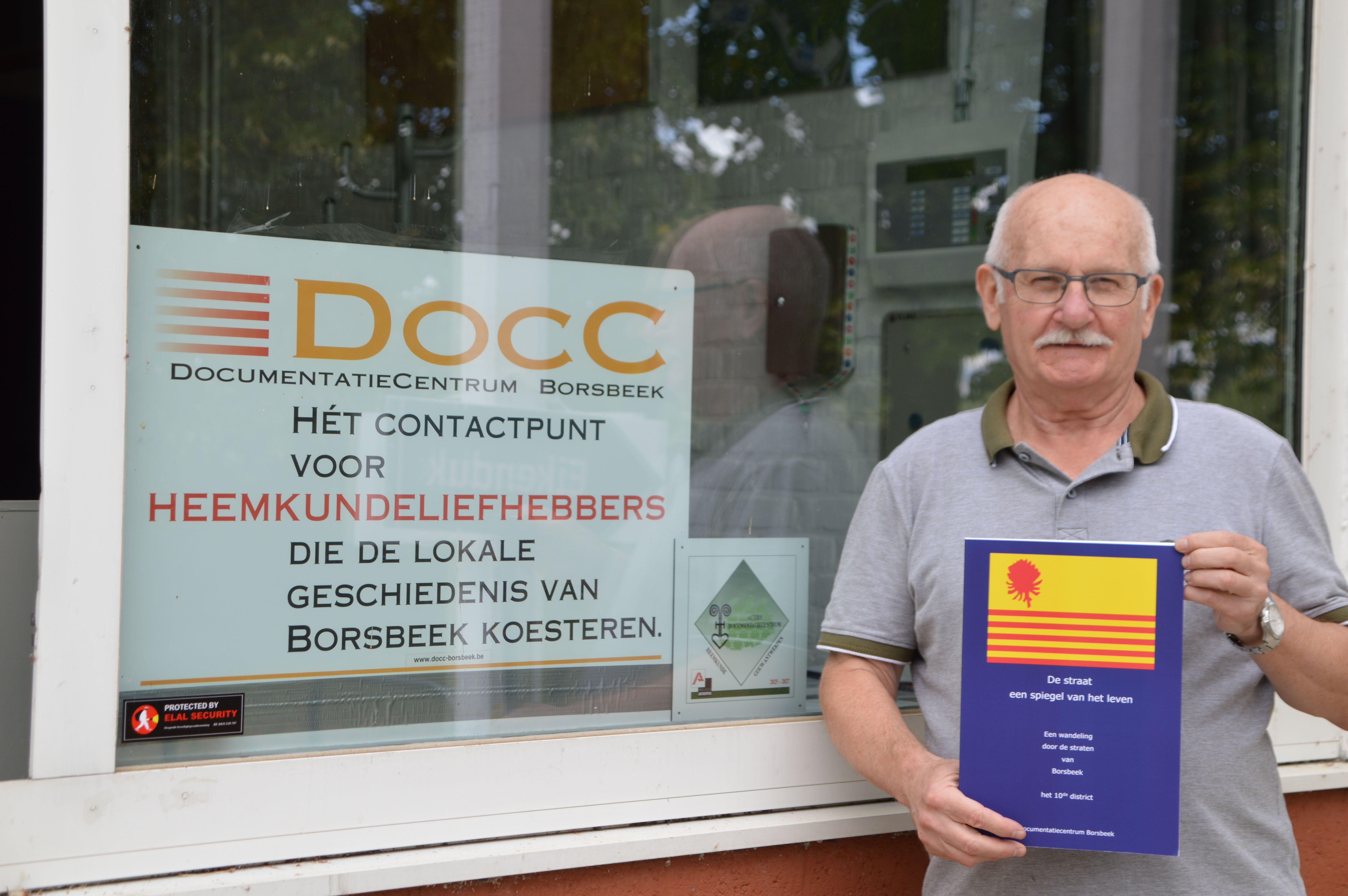 Vrijwilliger poseert voor een foto bij een bordje van Borsbeekse documentatiecentrum DocC